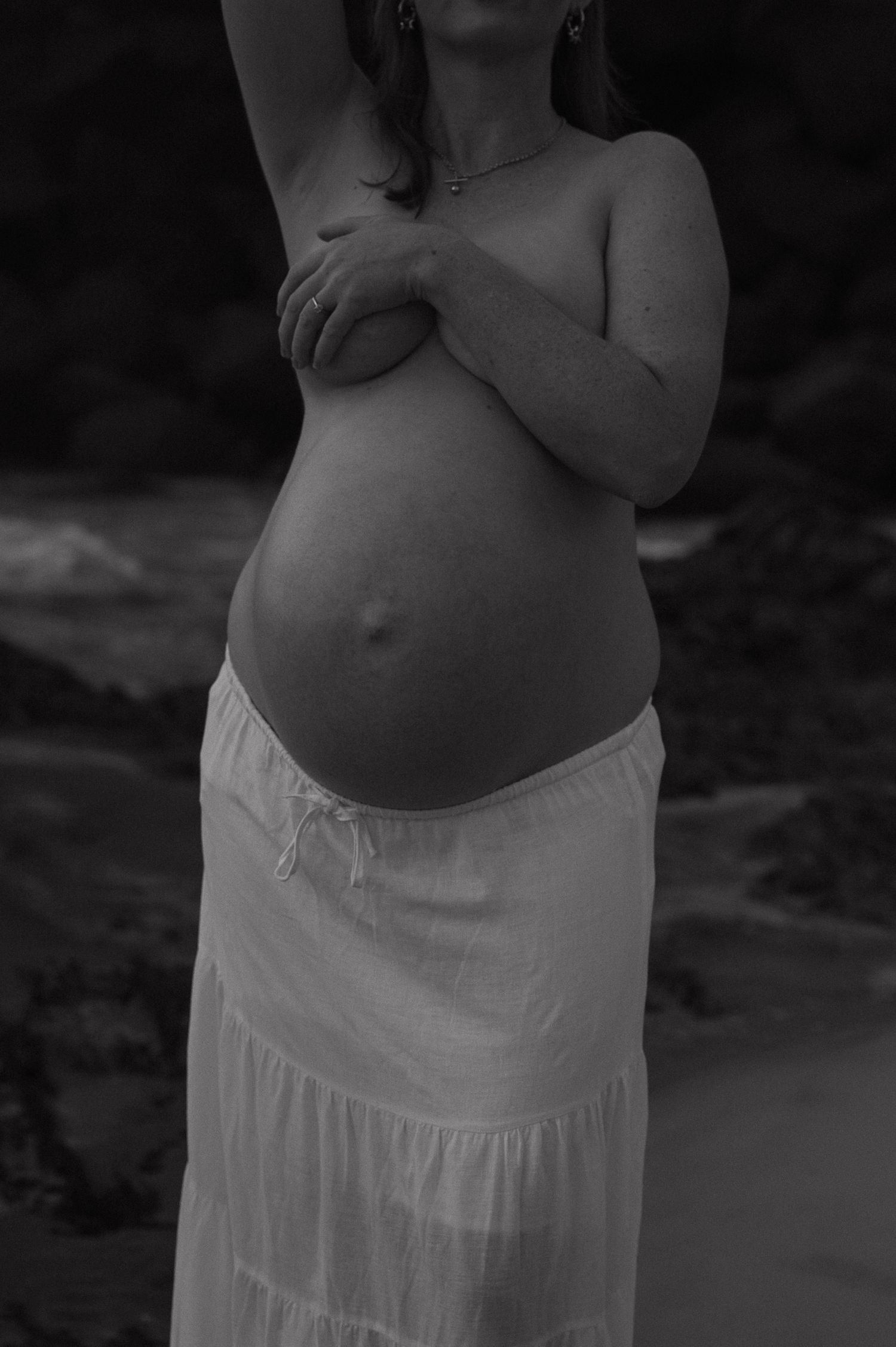 Maternity silhouette in white dress against dark beach background.