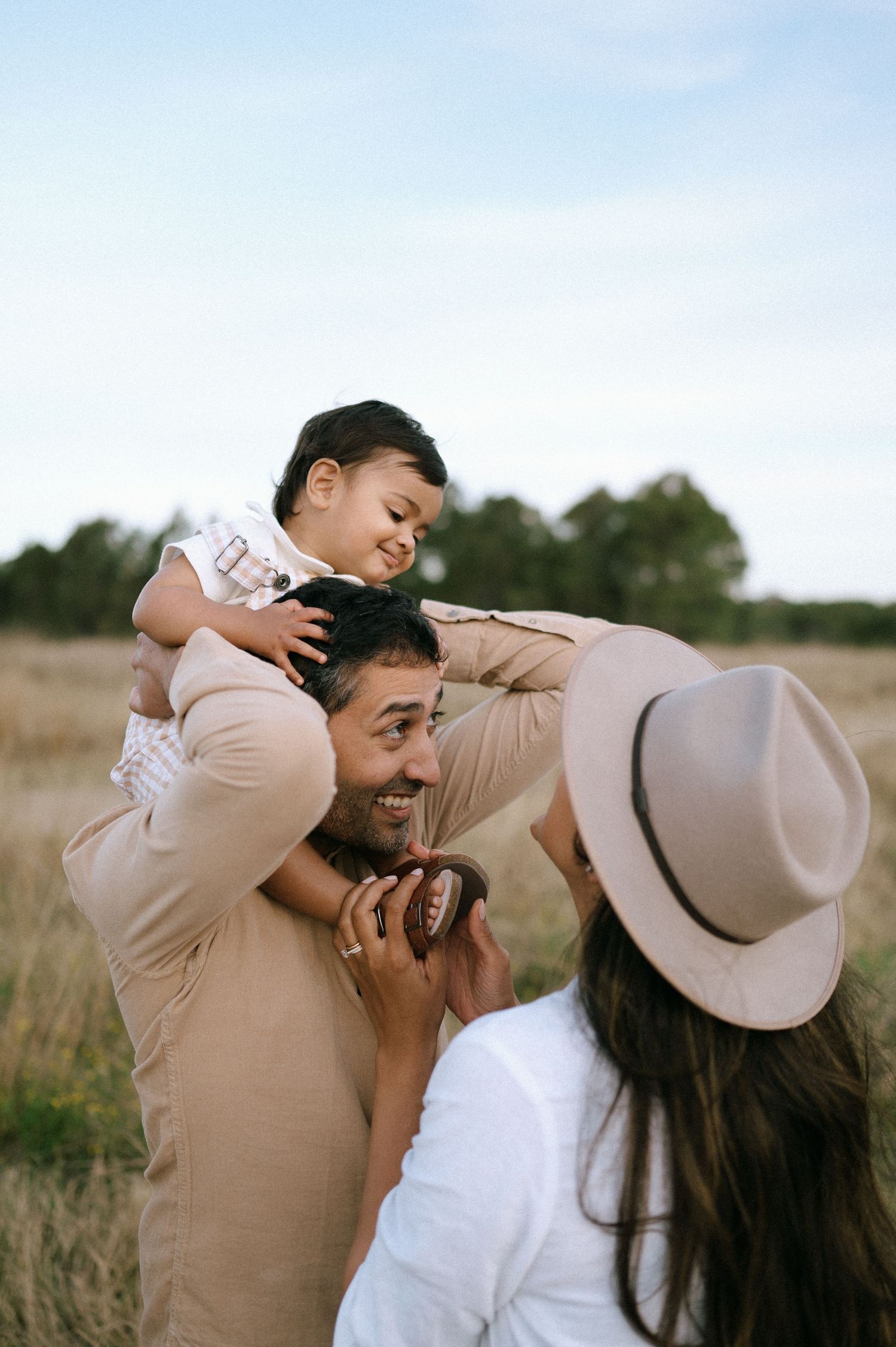 Family sharing playful moment in field with person wearing hat.