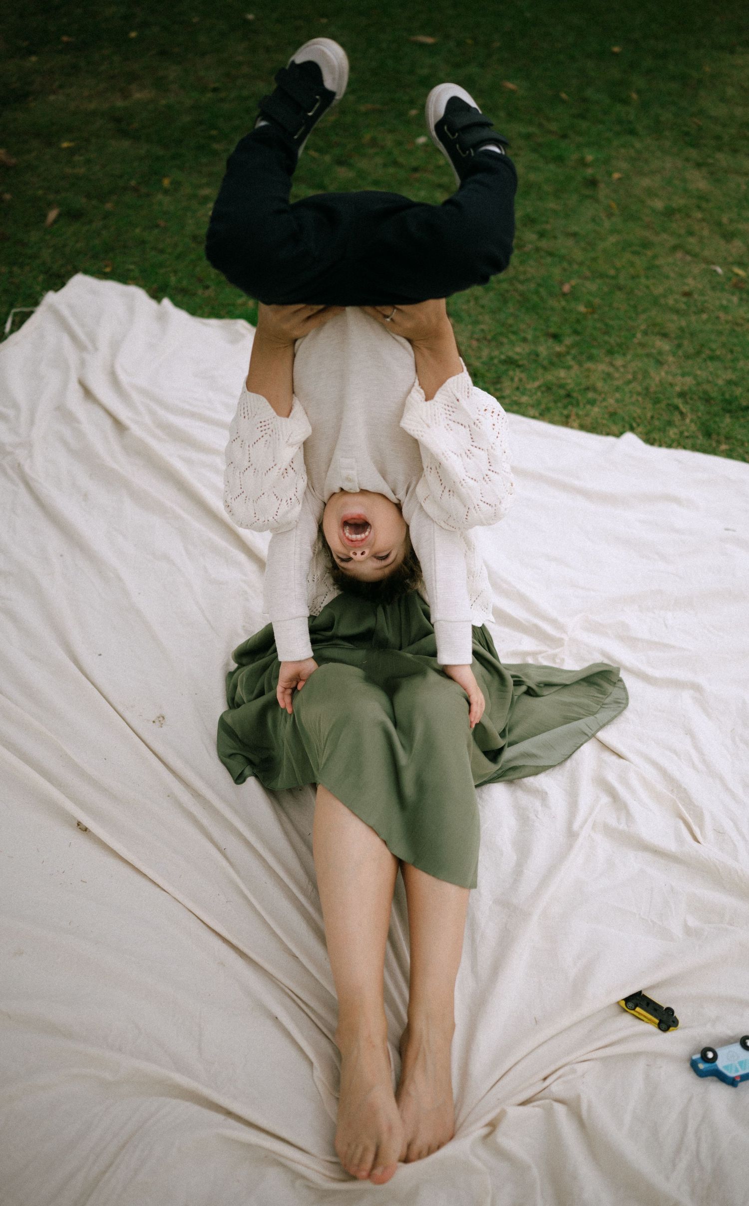 A person lying on a white blanket wearing an olive green dress and white top.