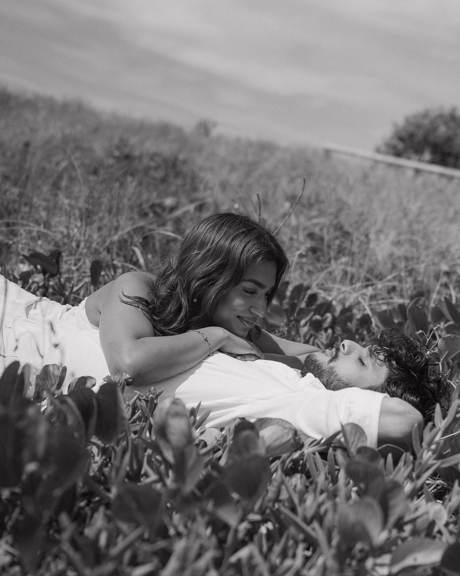A person in white lies peacefully in a field of flowers on a sunny day.