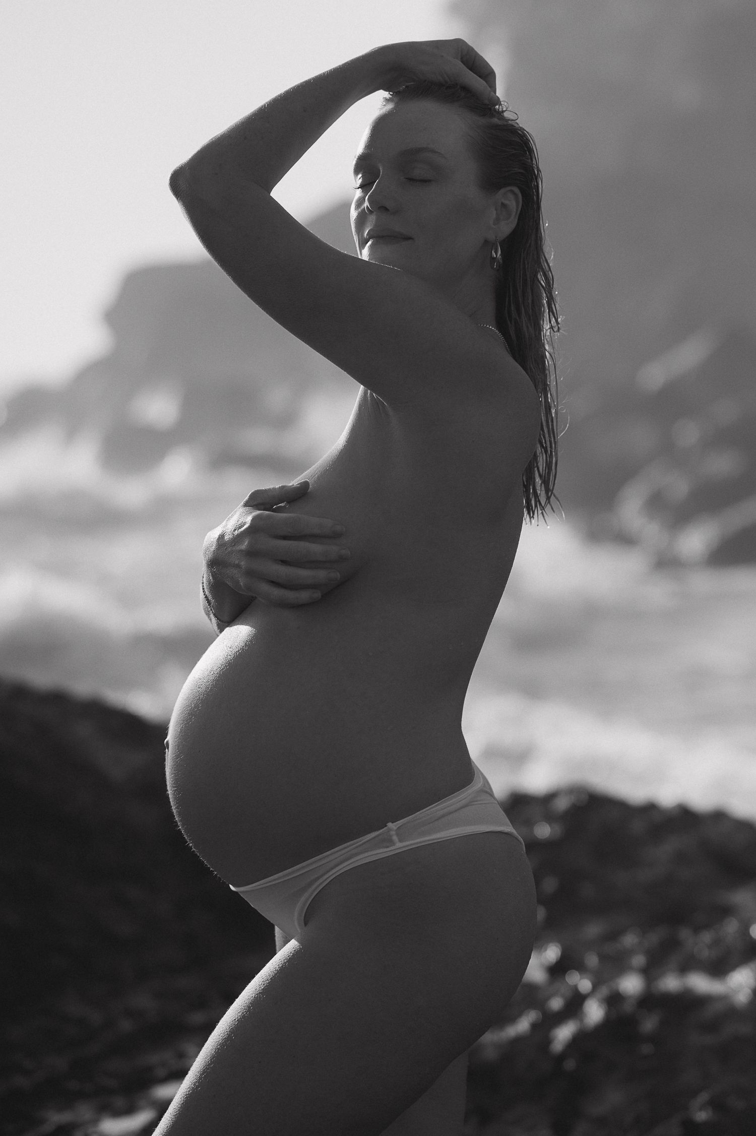 Artistic black and white maternity portrait against natural outdoor backdrop.