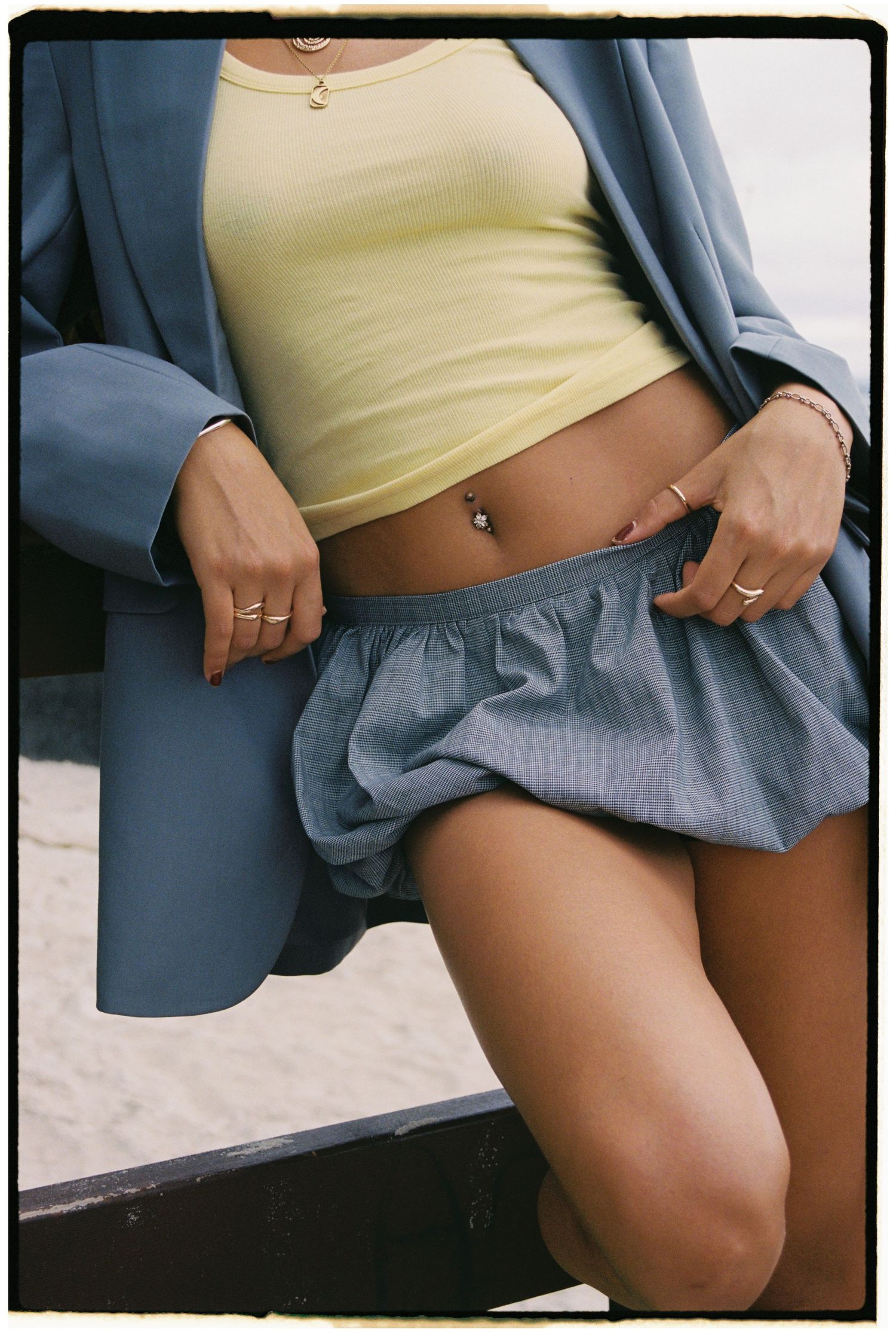 Close-up fashion detail of yellow crop top and blue blazer with pleated skirt.