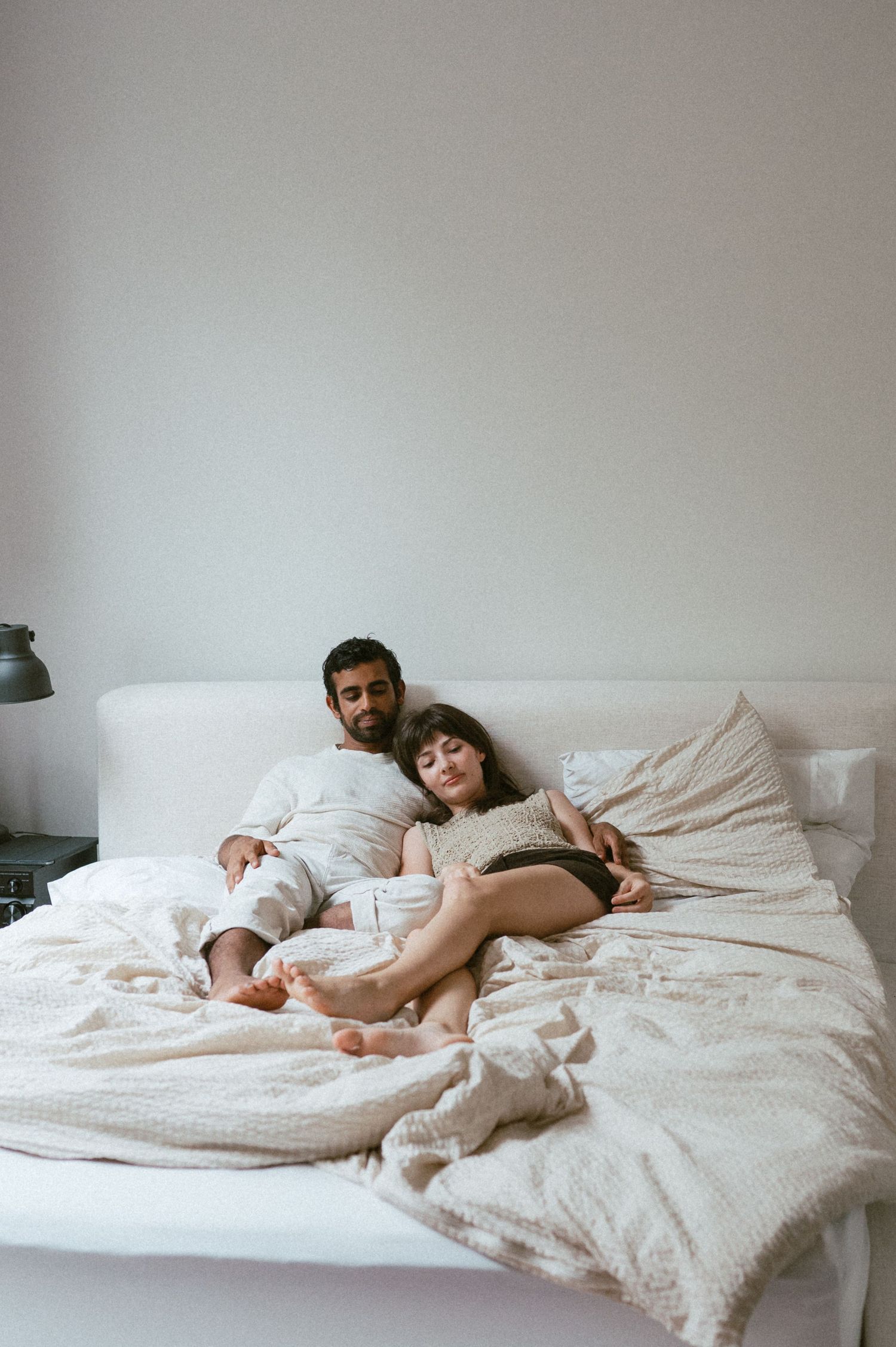 A couple relaxes together under white sheets in a minimalist bedroom.