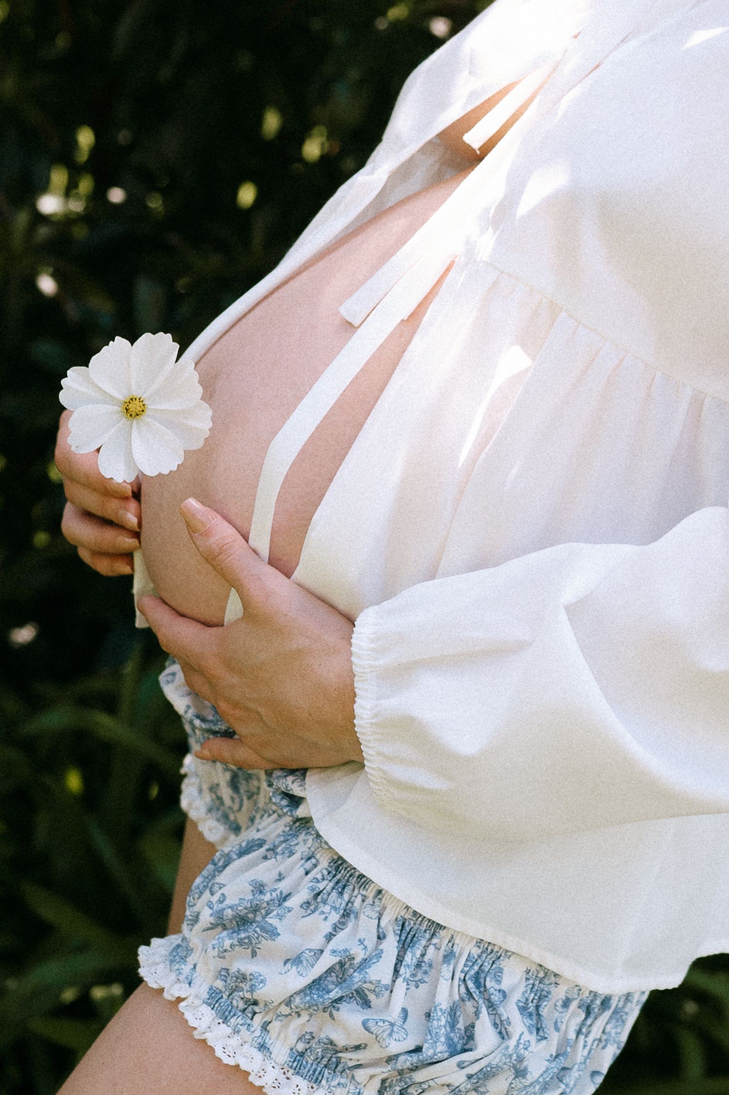 Maternity photo with white flowing top and floral skirt holding daisy flower.