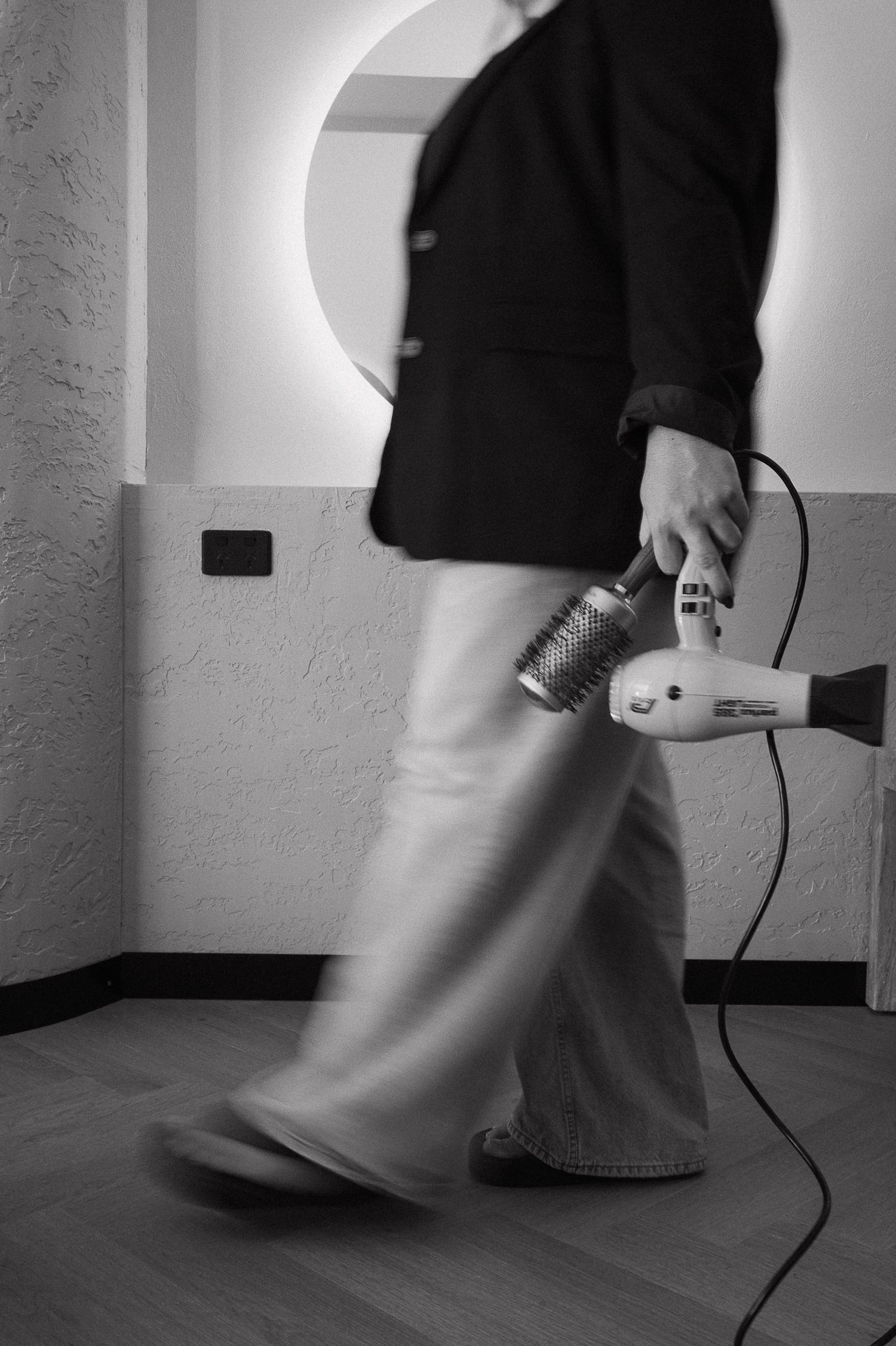 Black and white photo of a person walking with a hair dryer and round brush, motion blur on boots.