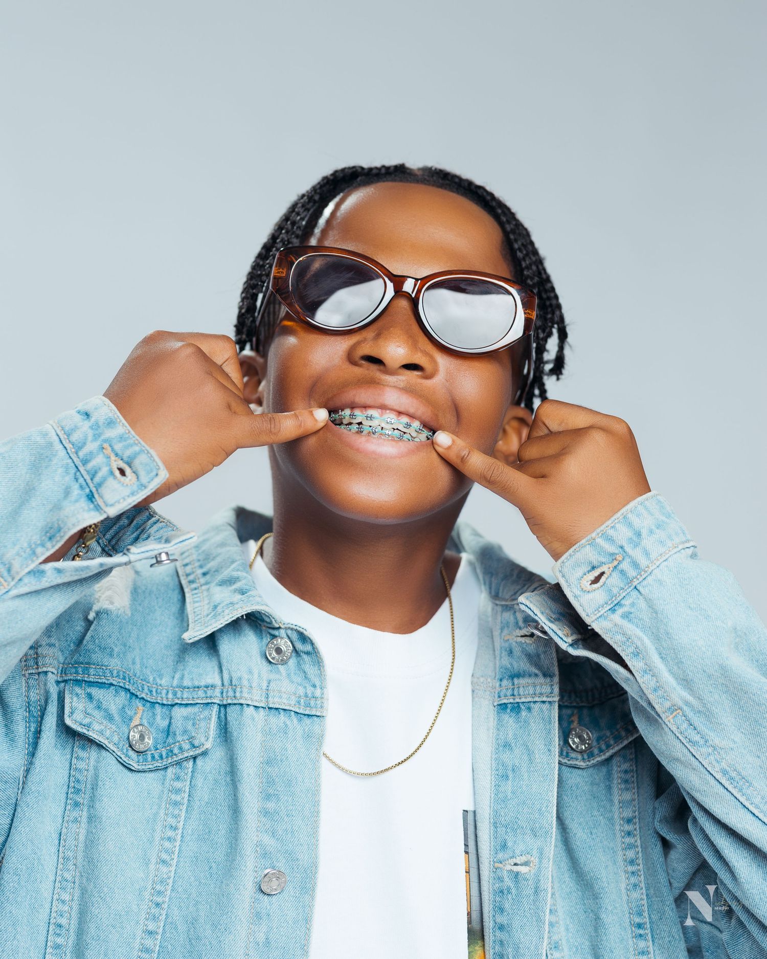 Person in braces wearing light denim jacket, metallic glasses and headphones shown in multiple artistic poses against gray backdrop.