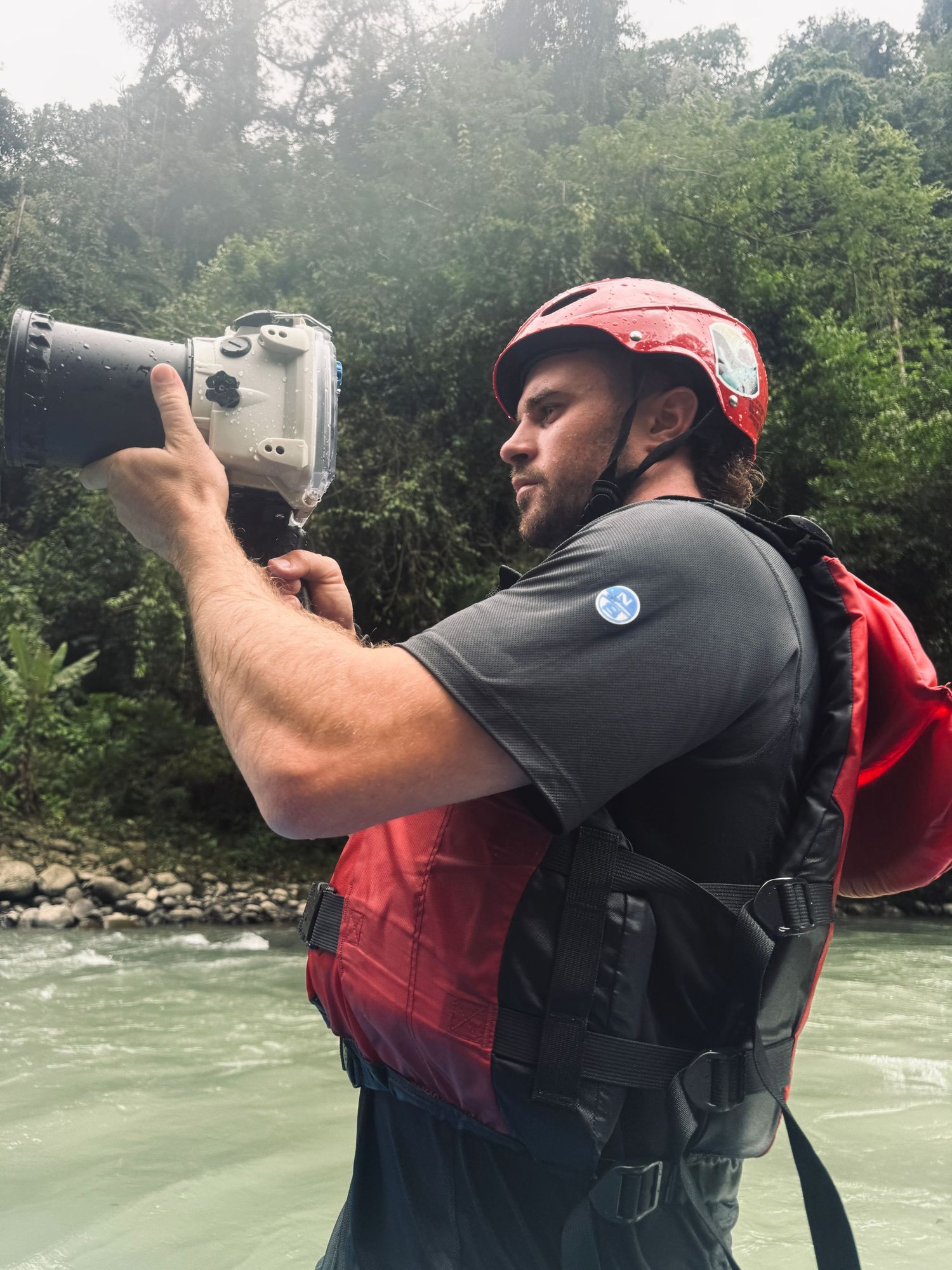 Photographer with backpack taking pictures near a rushing river.