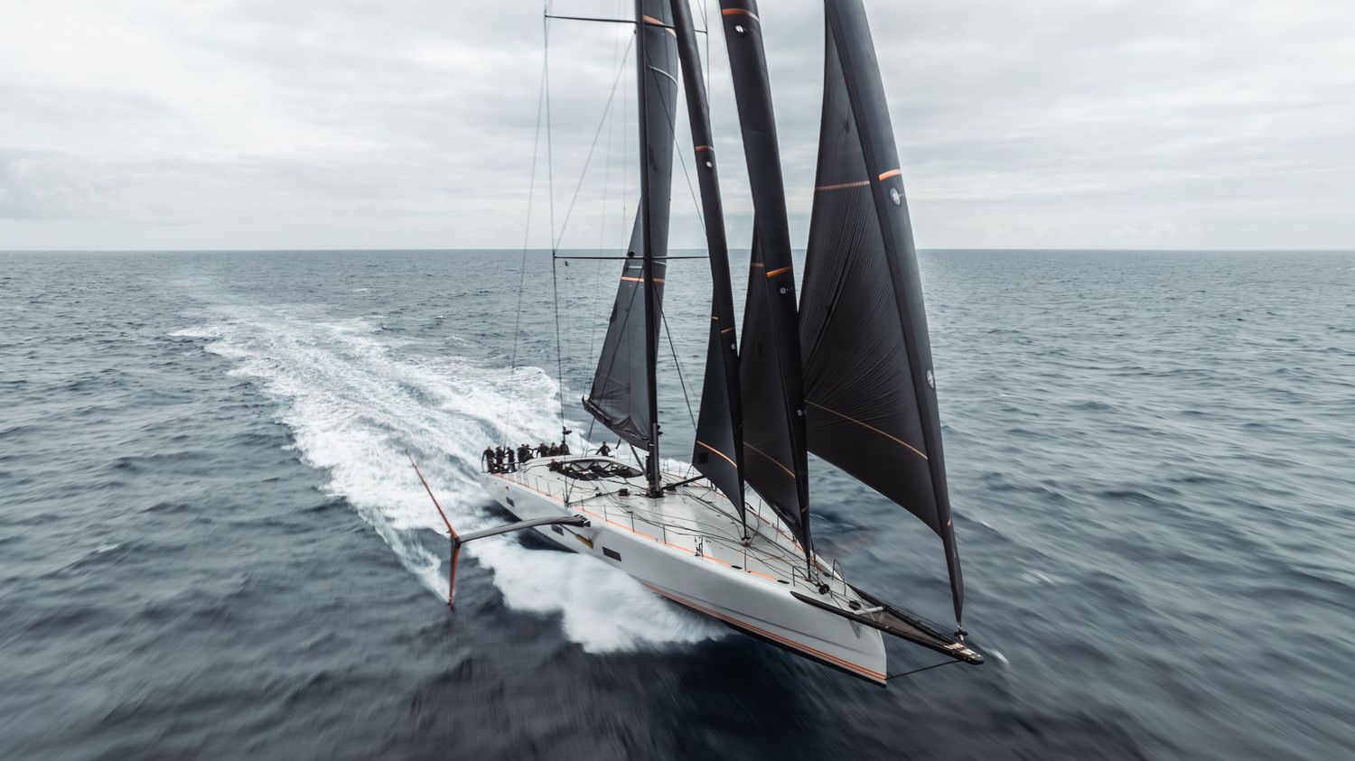 High-performance sailing yacht with black sails cutting through ocean waves at high speed.