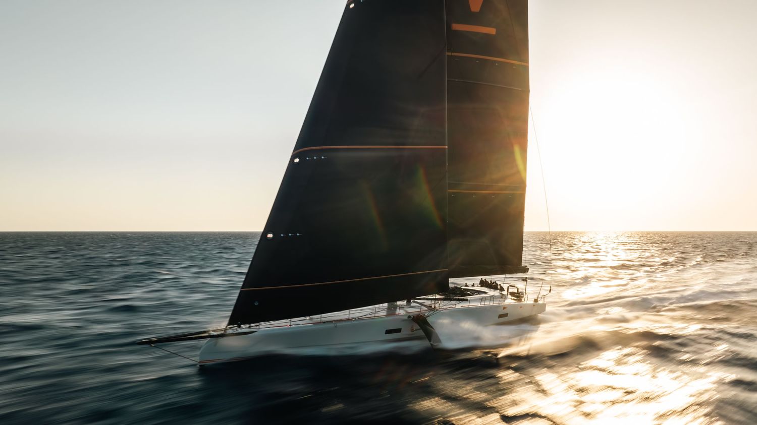 Sailboat glides across sparkling ocean waters during golden sunset with black sail catching wind.