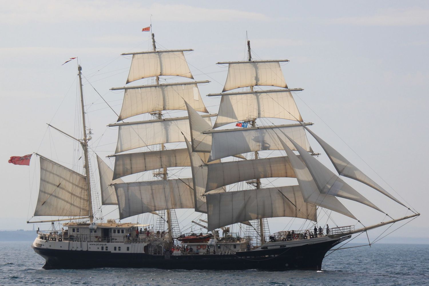 Tall sailing ships with white sails unfurled against a cloudy sky.