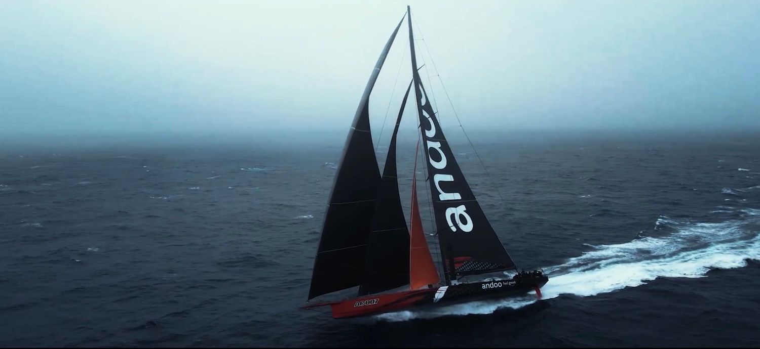 A sailboat races through choppy ocean waters with dark storm clouds looming in the background.