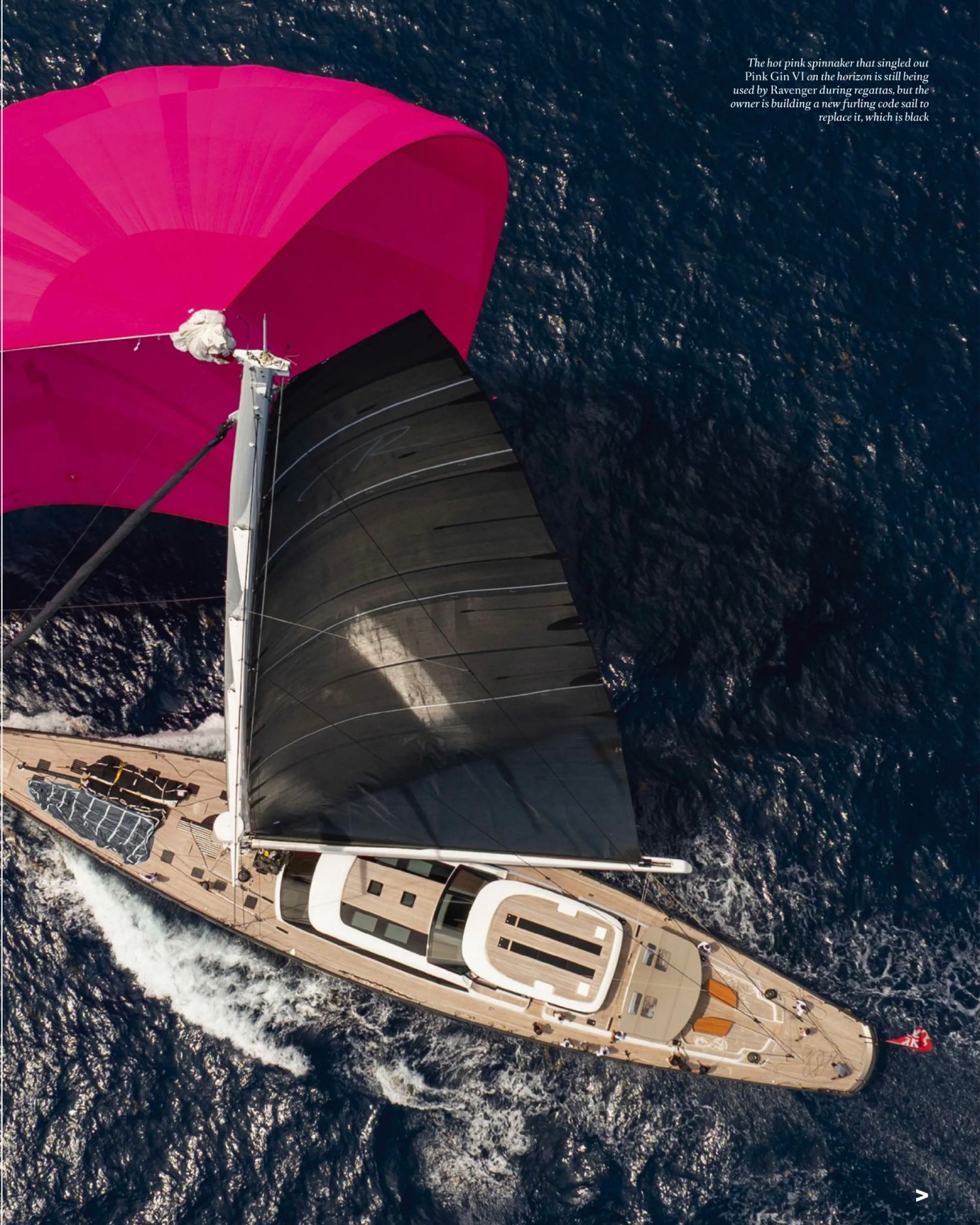 Aerial view of a luxury sailing yacht with distinctive pink sails cruising through dark blue ocean waters.