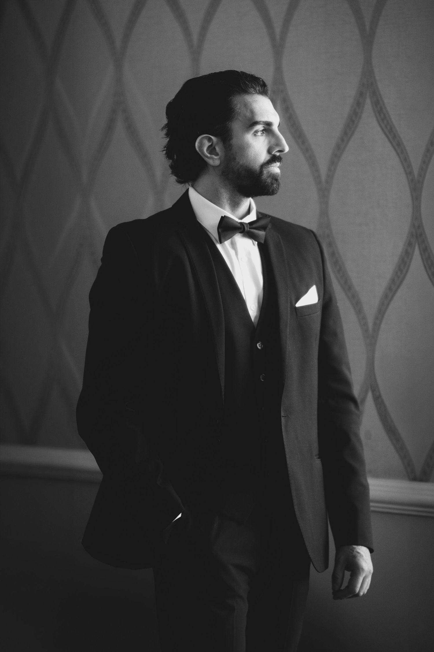 Black and white portrait of a bearded man in a tuxedo with bow tie and pocket square, gazing thoughtfully to the side.