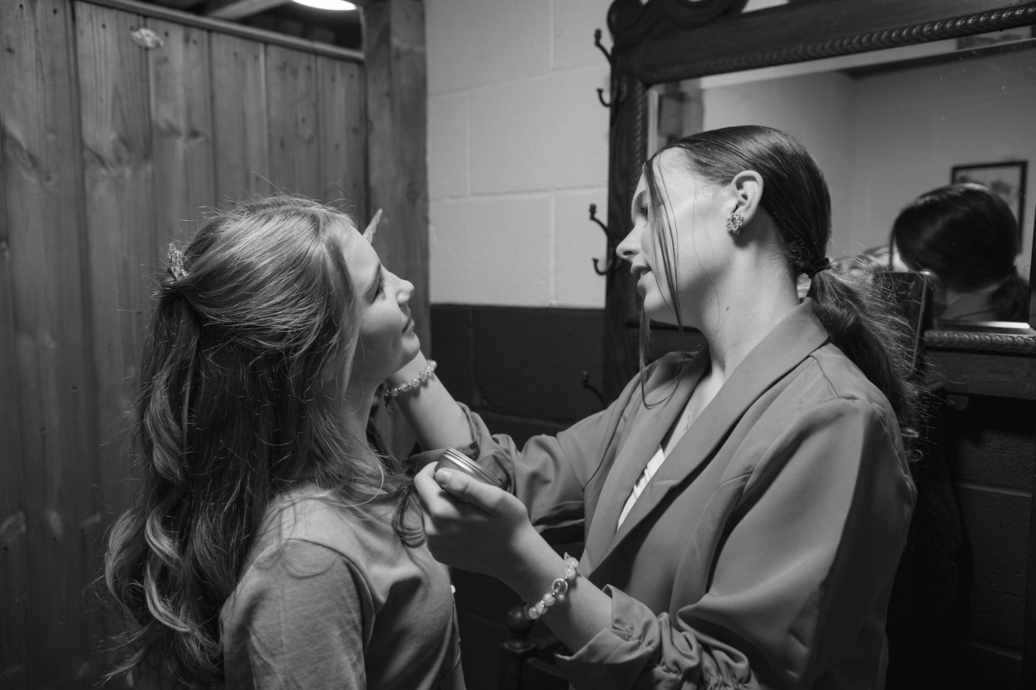 Black and white photo of a makeup artist applying lipstick to a bride in front of a mirror.