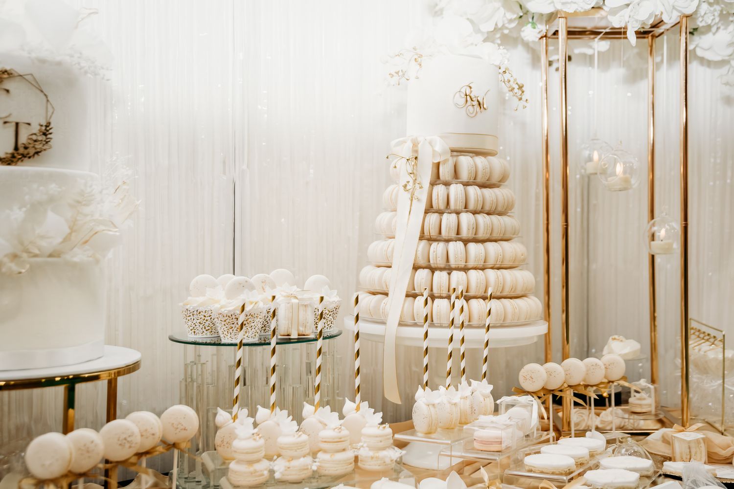 Elegant white and gold wedding dessert table featuring macarons tower, cake pops, and meringues.