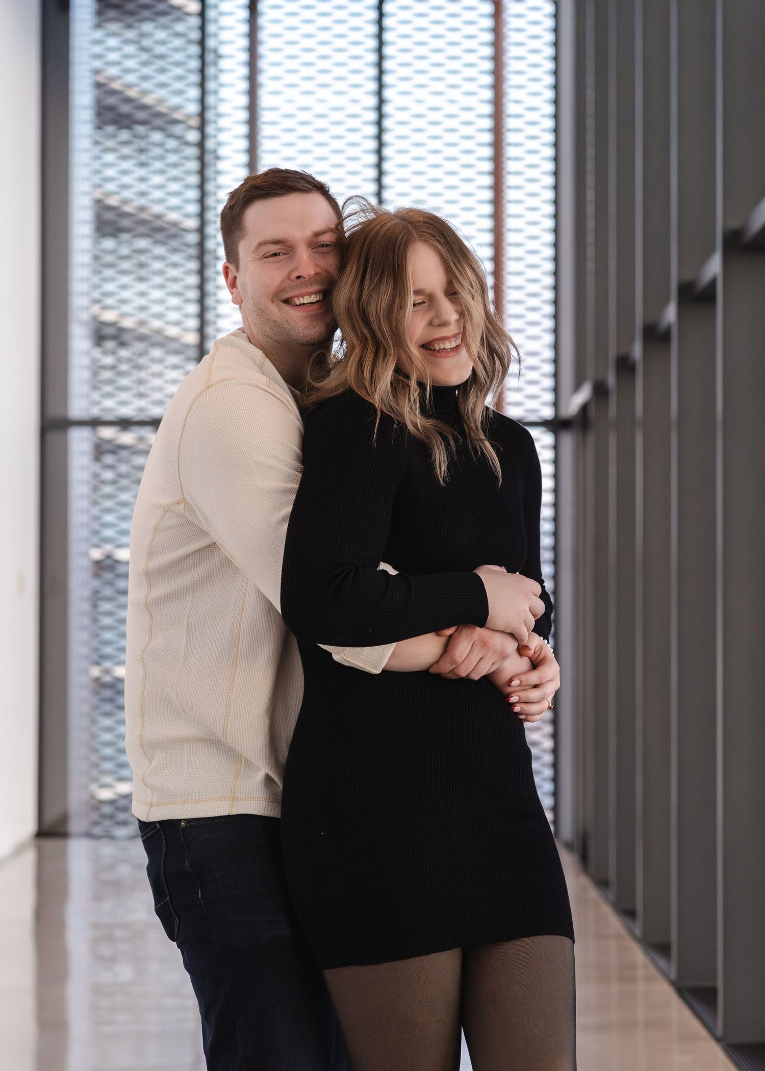 Two figures embracing in a bright white hallway.