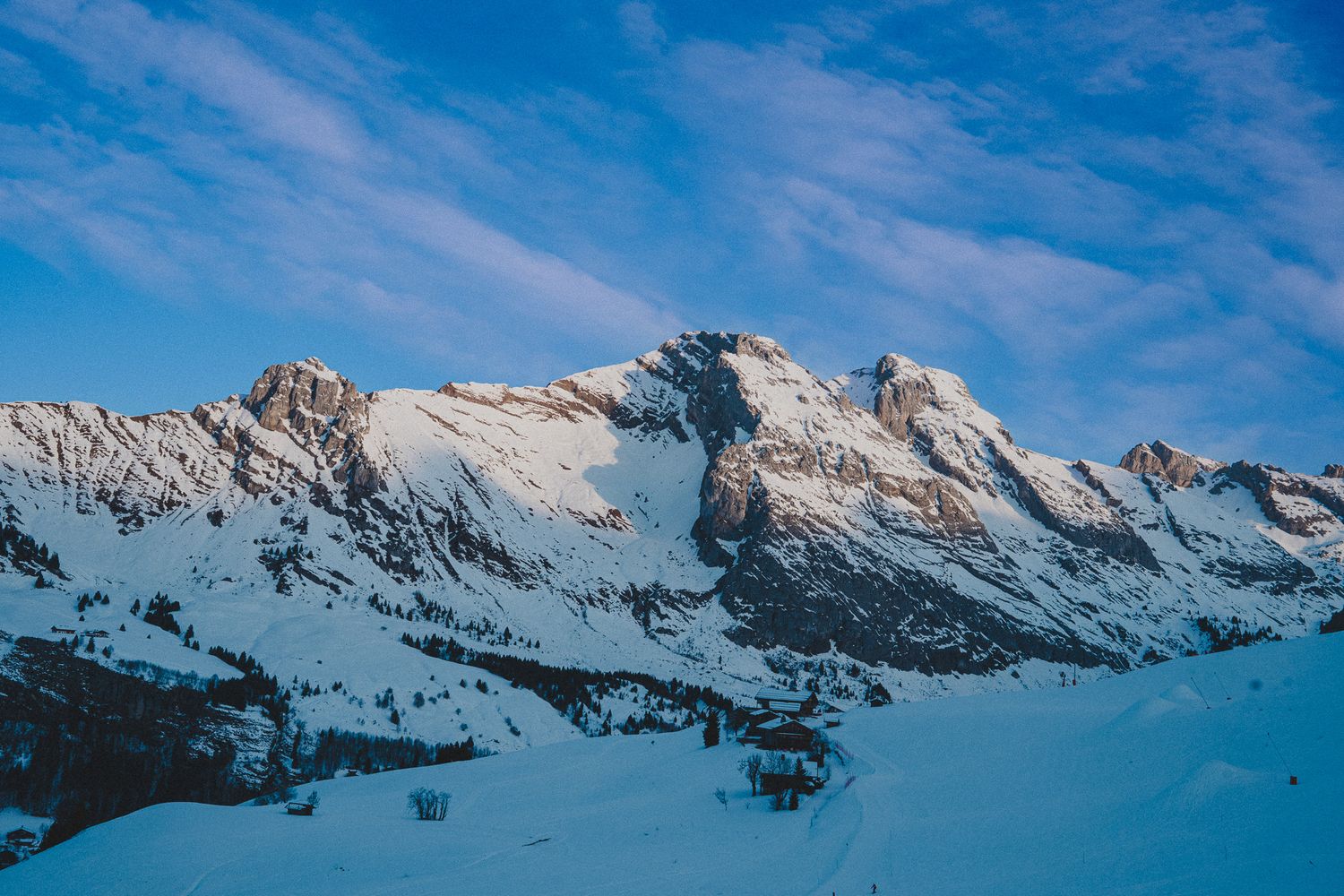 Snow-covered mountain peaks rise against a vibrant blue sky in a dramatic winter alpine landscape.