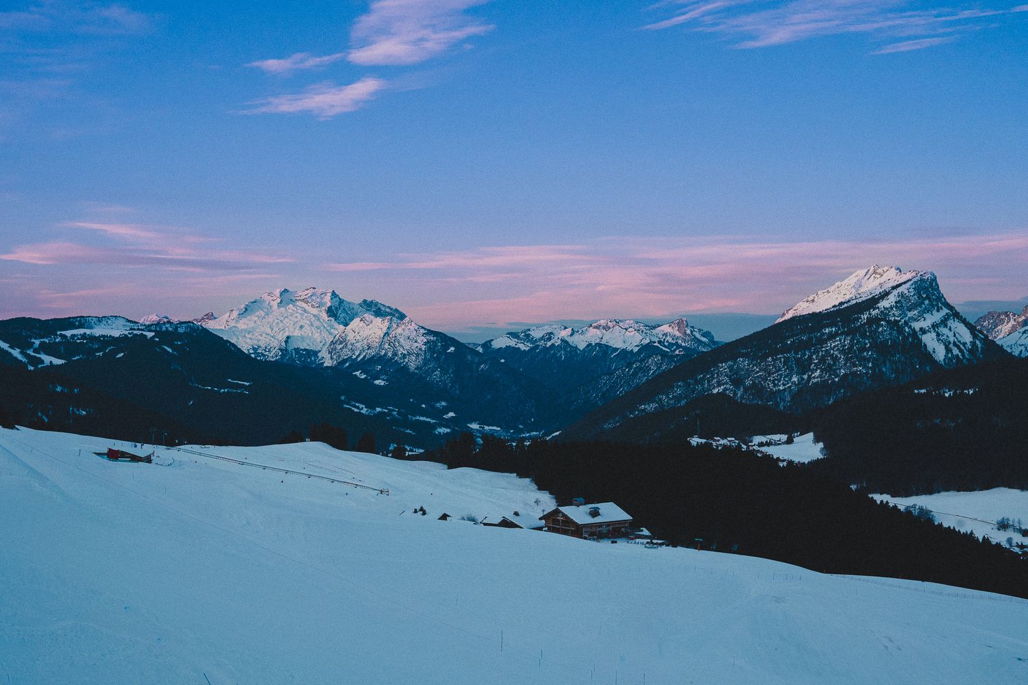 Panoramic winter landscape showing snow-covered mountains and blue sky stretching across multiple connected photos.