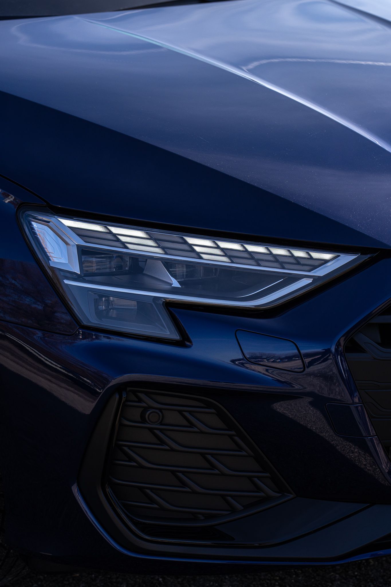 Close-up detail shots of a sleek dark blue car's modern LED headlight design and front fascia elements.
