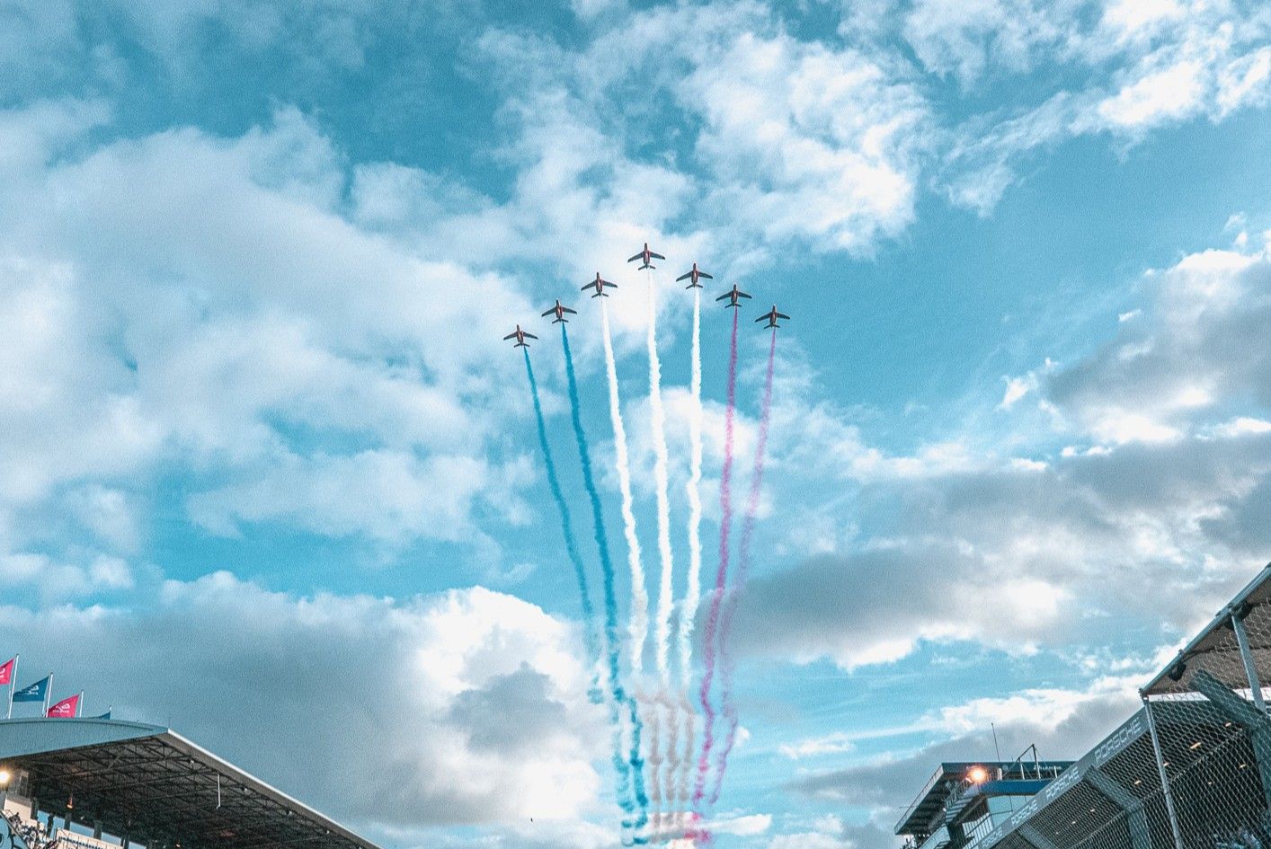 Military jets perform aerial maneuvers leaving colorful smoke trails against a bright blue sky with white clouds.
