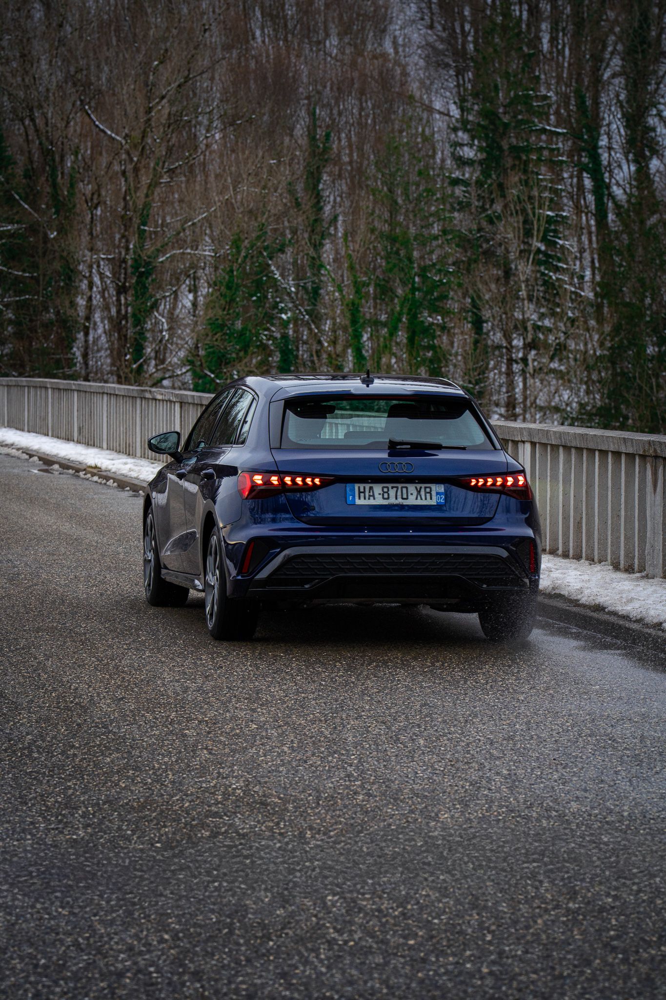 Rear view of a sleek blue Audi RS e-tron GT electric vehicle parked on a snowy forest road.