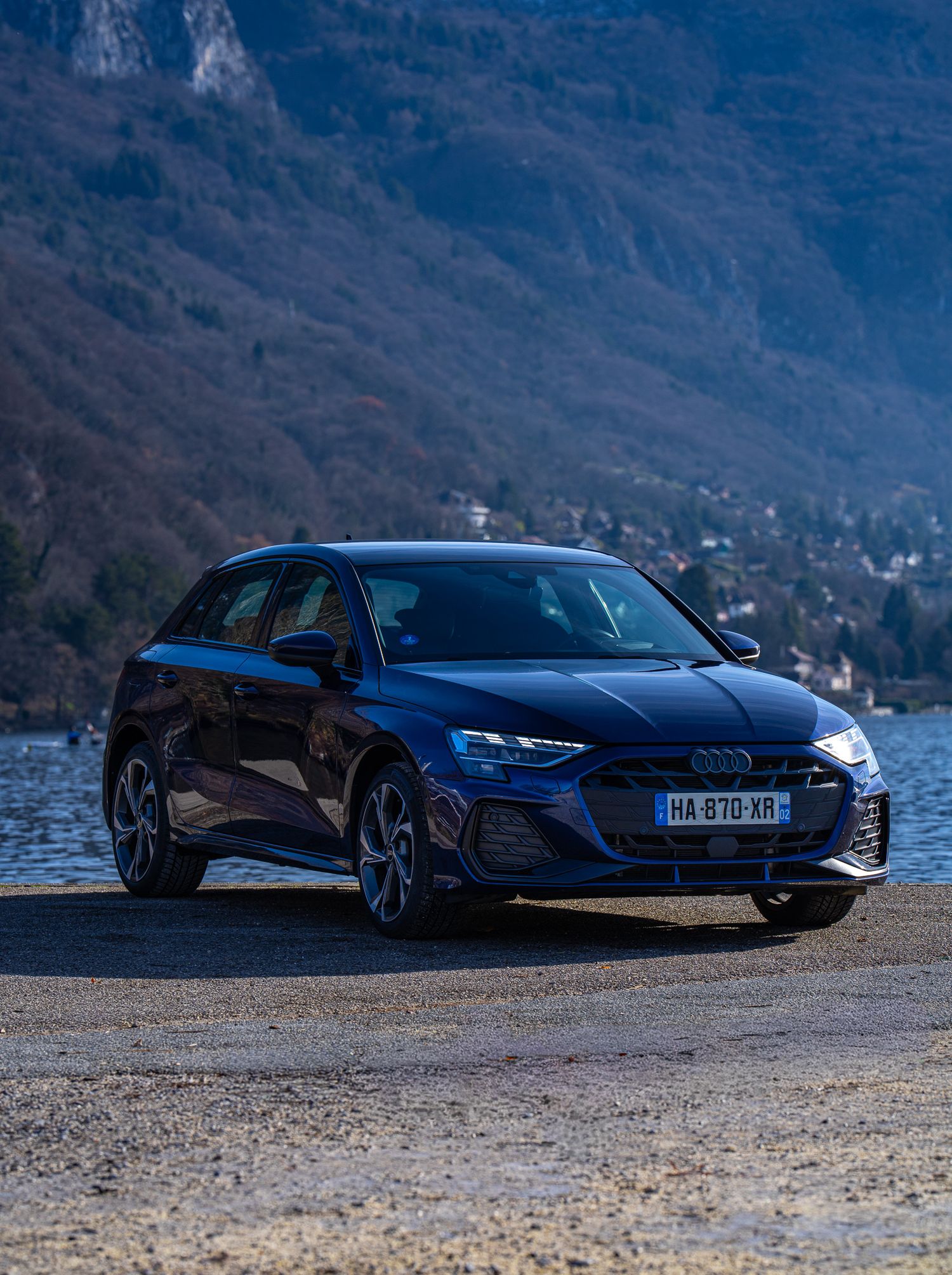 Black Audi R8 supercar parked by a scenic mountain lake at sunset with dramatic lighting and reflections.