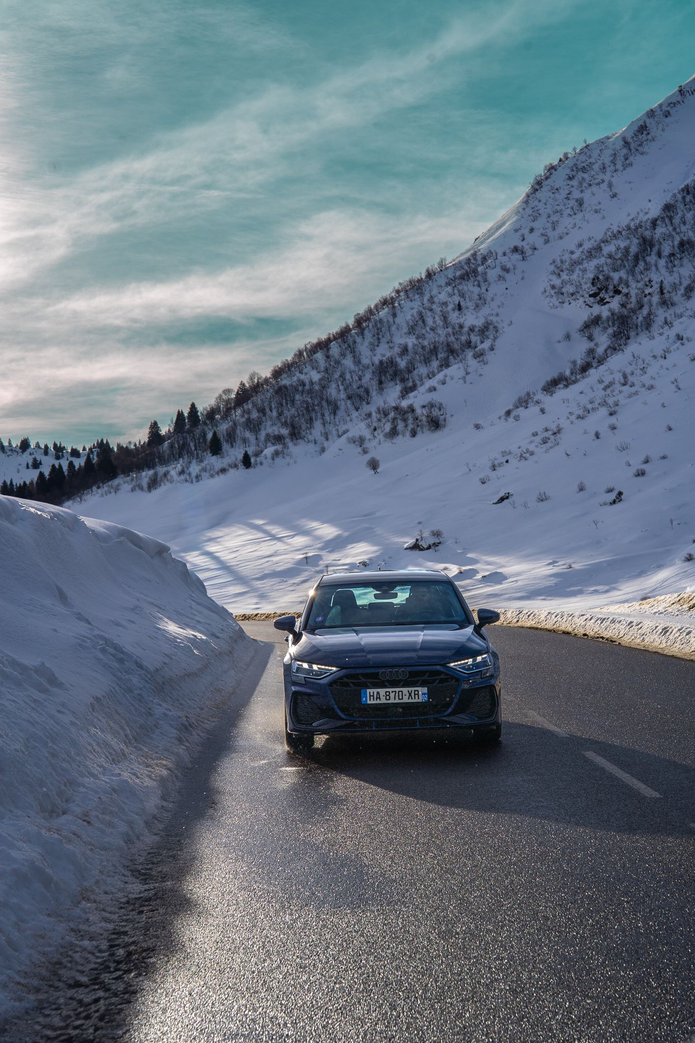 A black BMW M4 drives on a snowy mountain road with dramatic winter landscapes in the background.