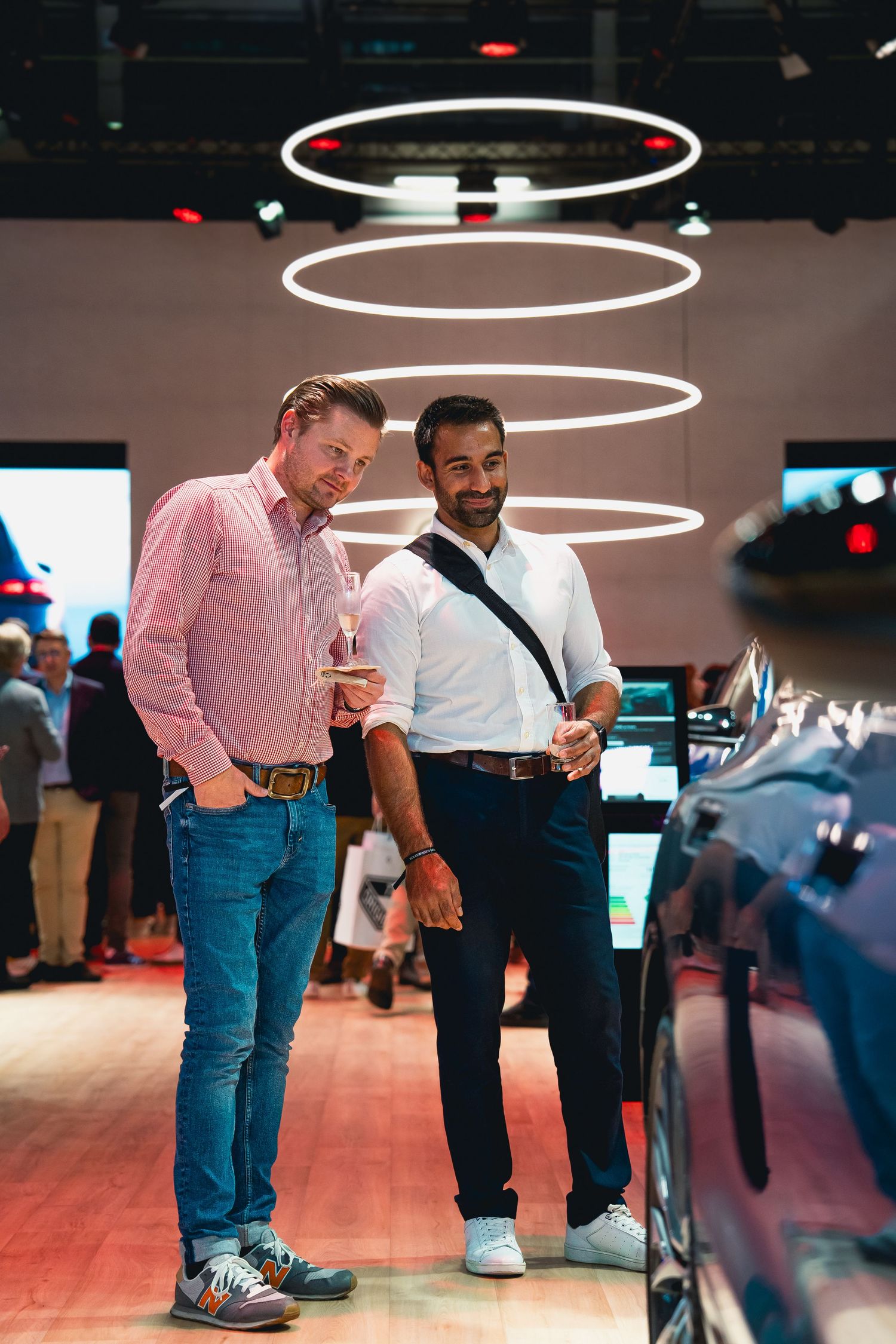 Two attendees viewing vehicles under modern circular lighting at Audi showroom display.
