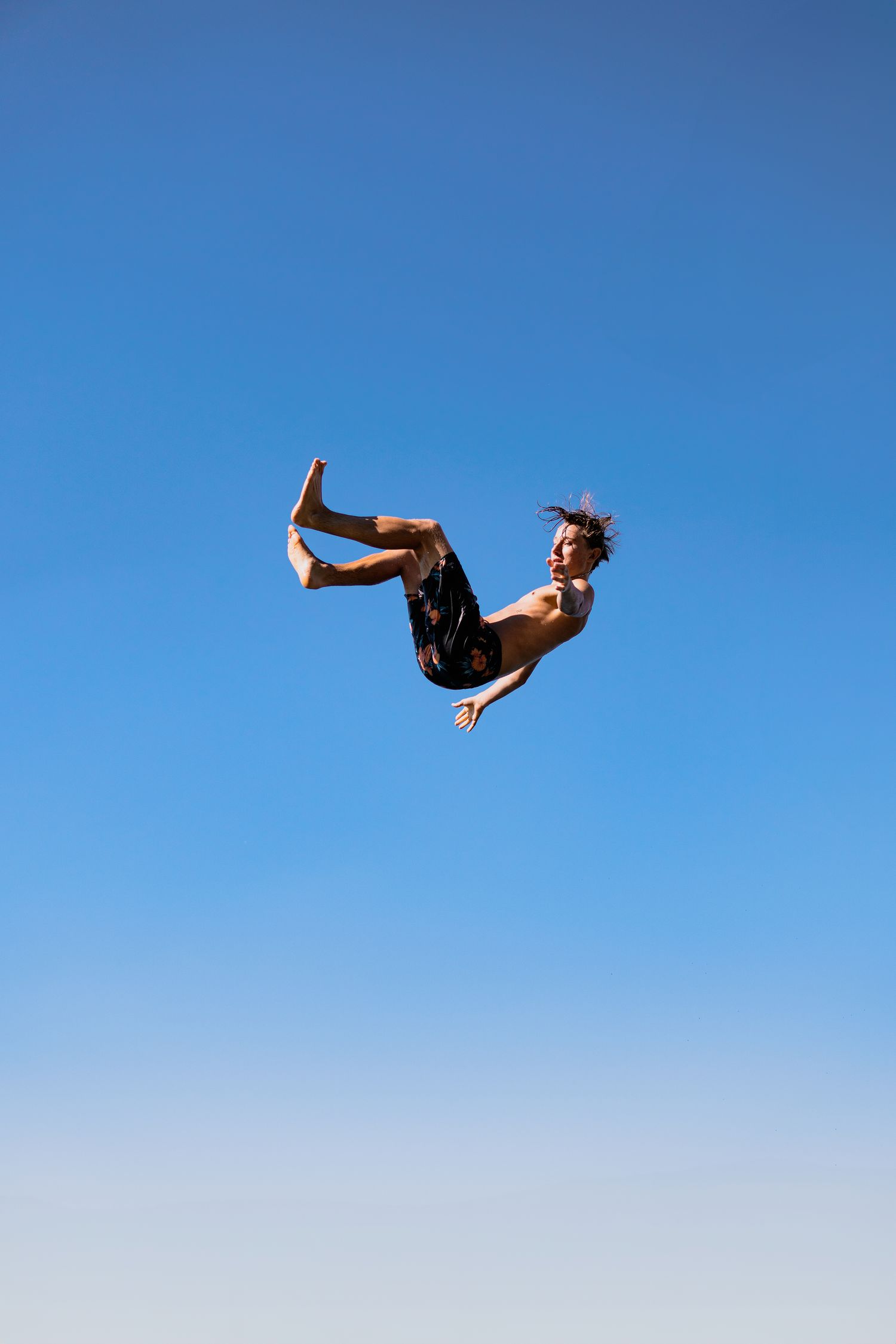 Silhouette of someone performing a backflip against a bright blue sky.