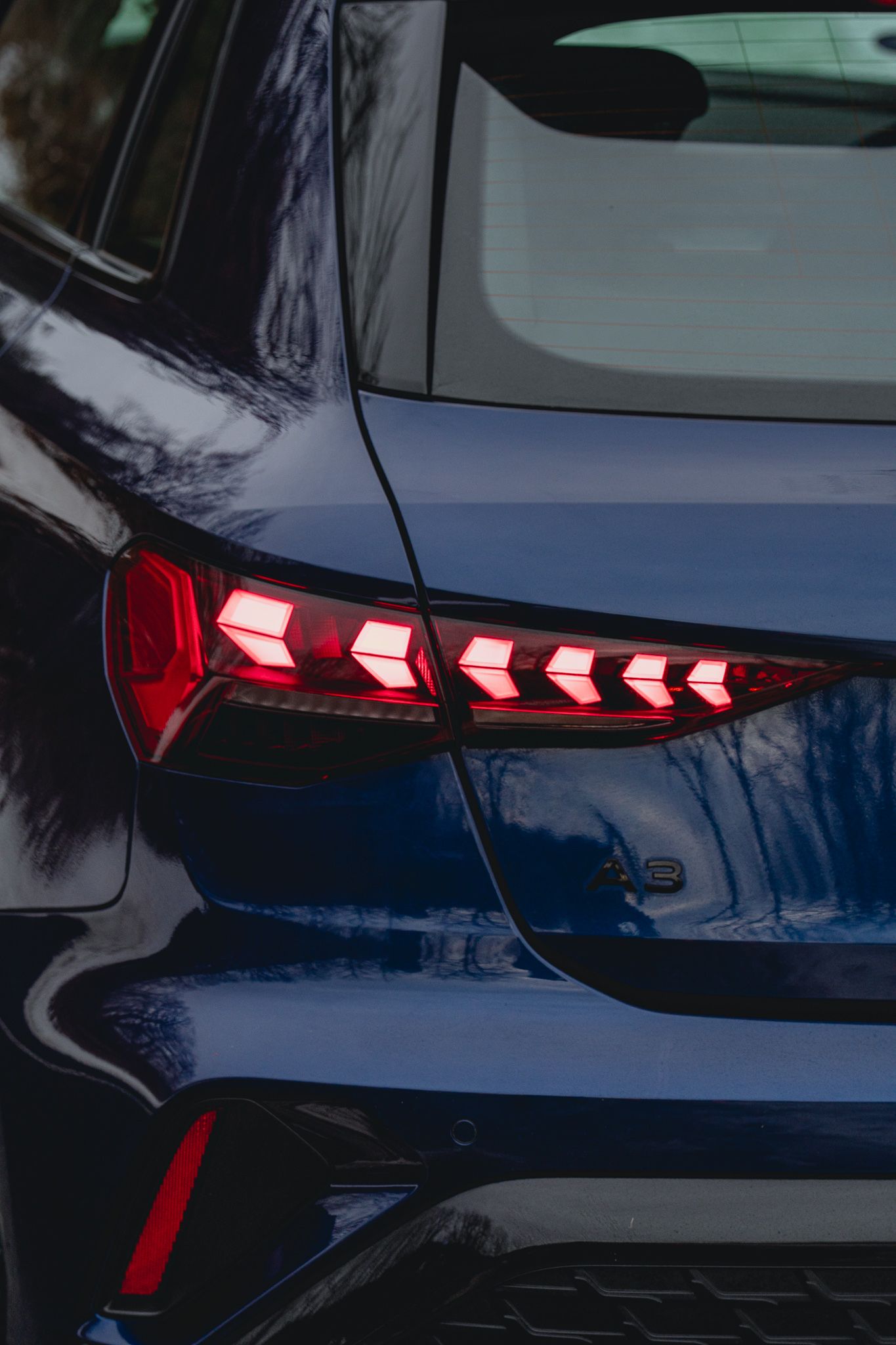Close-up view of modern LED taillights on a dark blue luxury car showing sequential lighting pattern.
