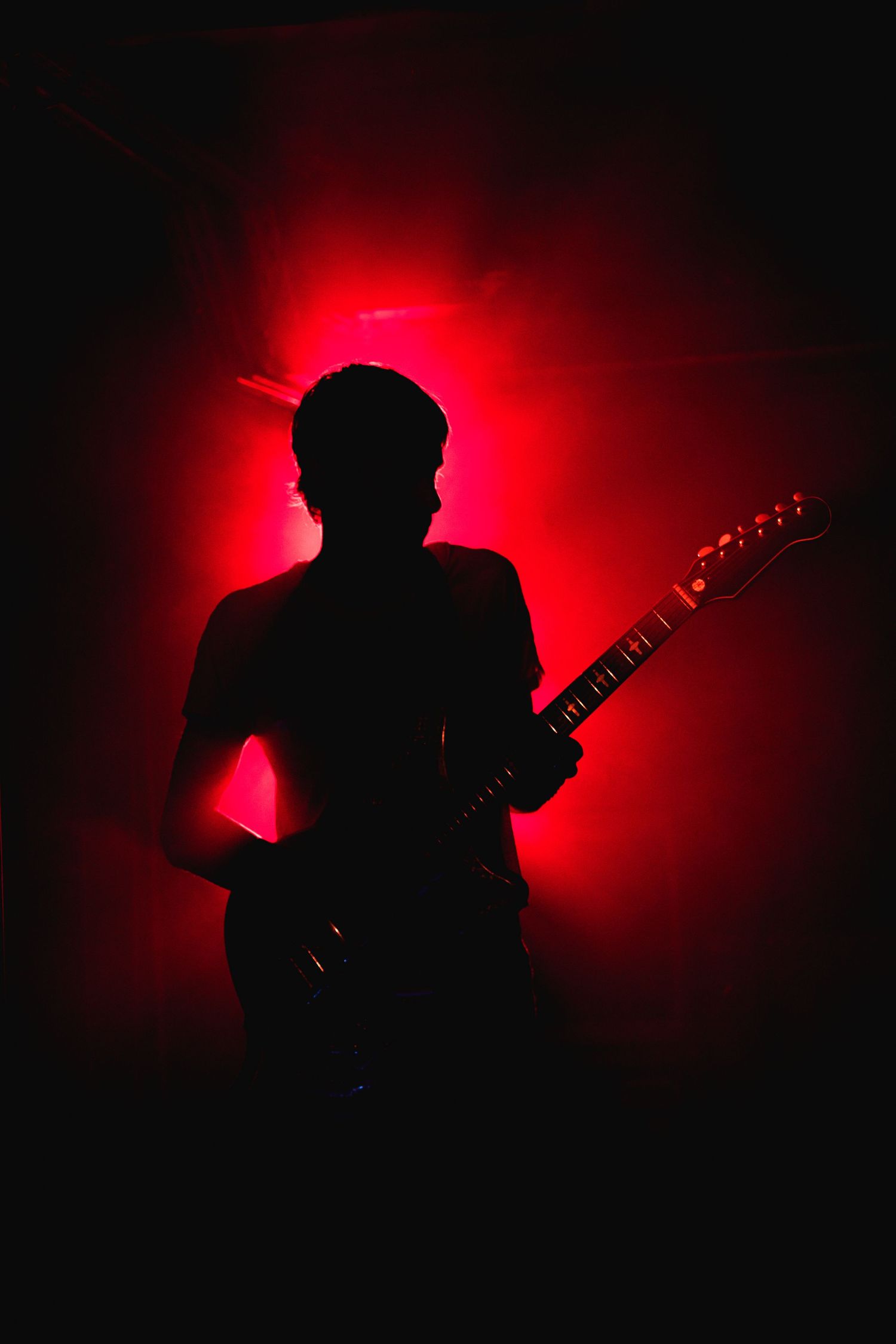 Silhouetted figure plays guitar against dramatic red backlit background during performance.