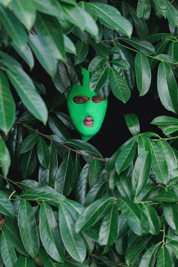 A bright green mask peeking through lush tropical foliage creates a mysterious and artistic composition.