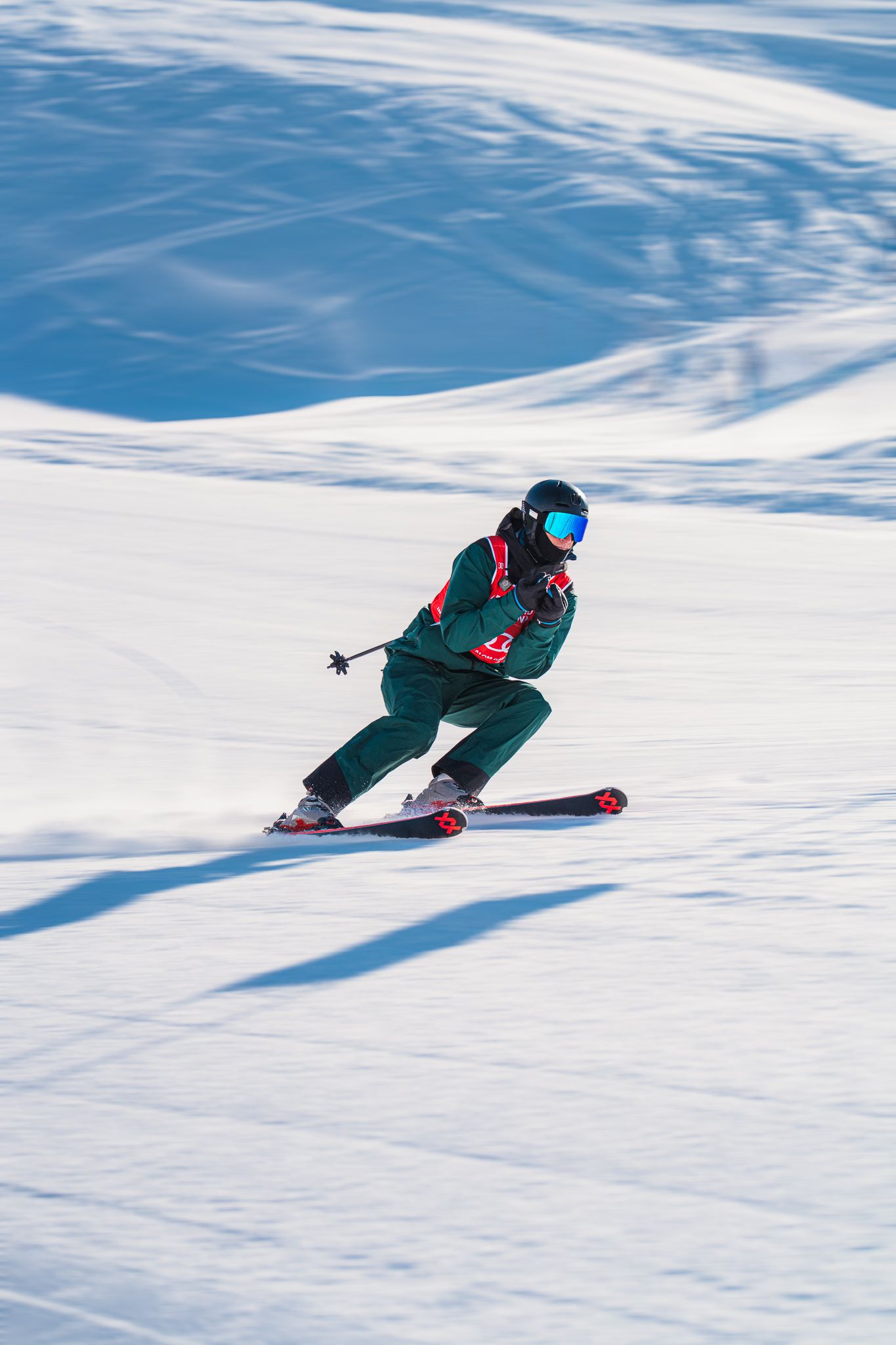 A skier carves through fresh powder snow on a sunny winter slope, creating dynamic turns in pristine conditions.