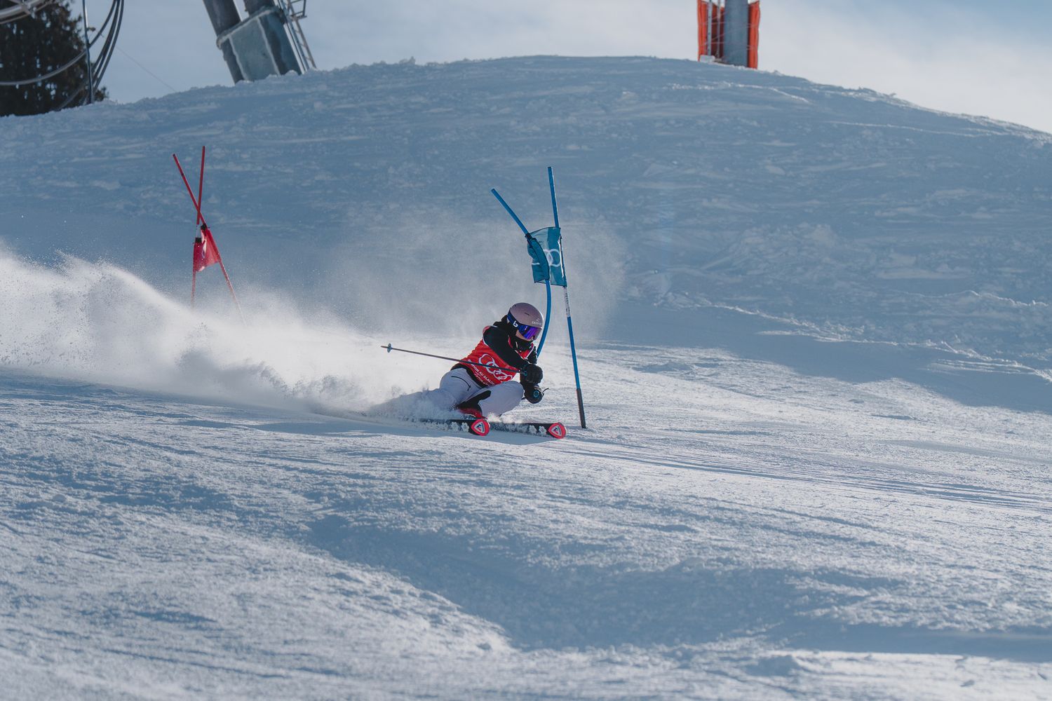Skier carves down snowy slope in dynamic parallel turn position while creating powder spray on mountain terrain.