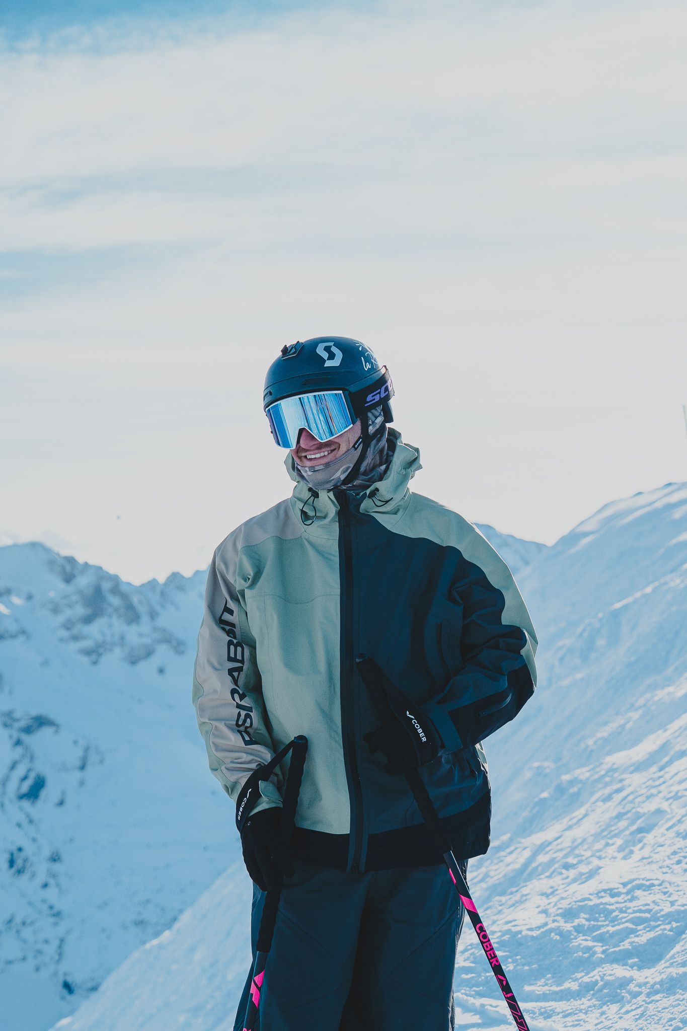 Skiers in winter gear stand against snowy mountain backdrop with bright blue sky on a clear day.