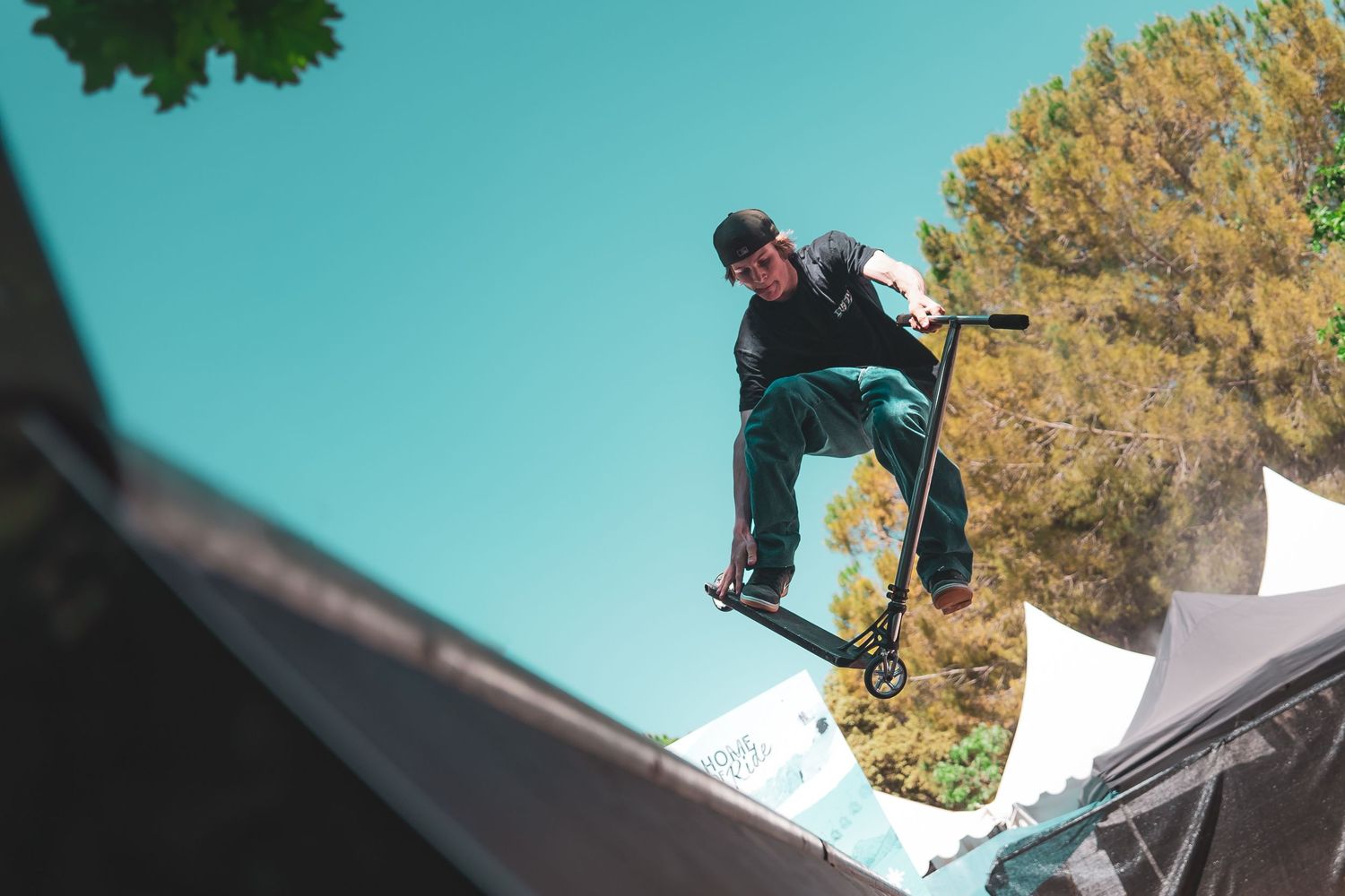 Snowboarder performing a high-flying aerial trick off a snow ramp against a blue sky and autumn trees in the background.