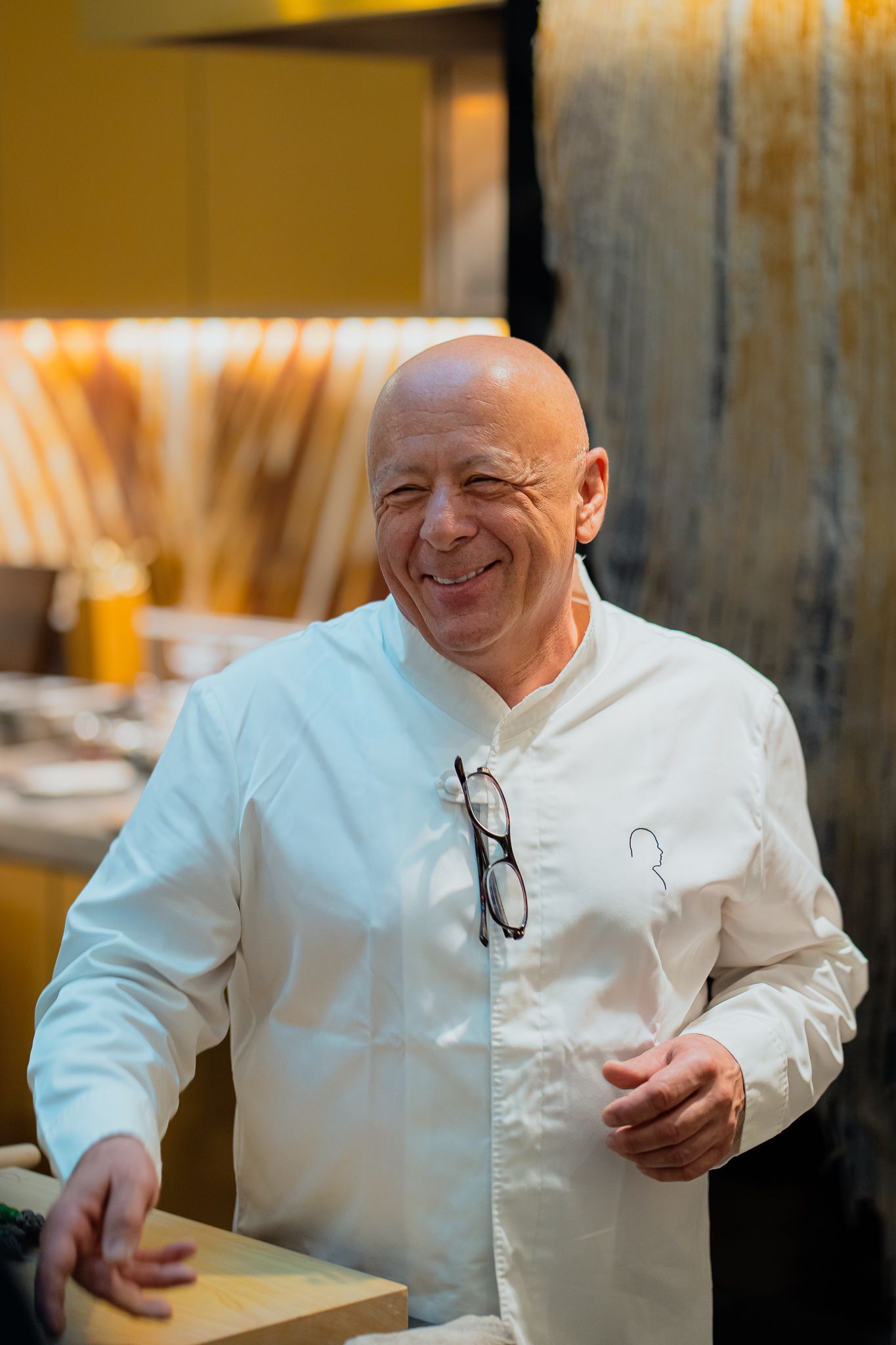 Chef in white uniform smiling while preparing food in restaurant kitchen.
