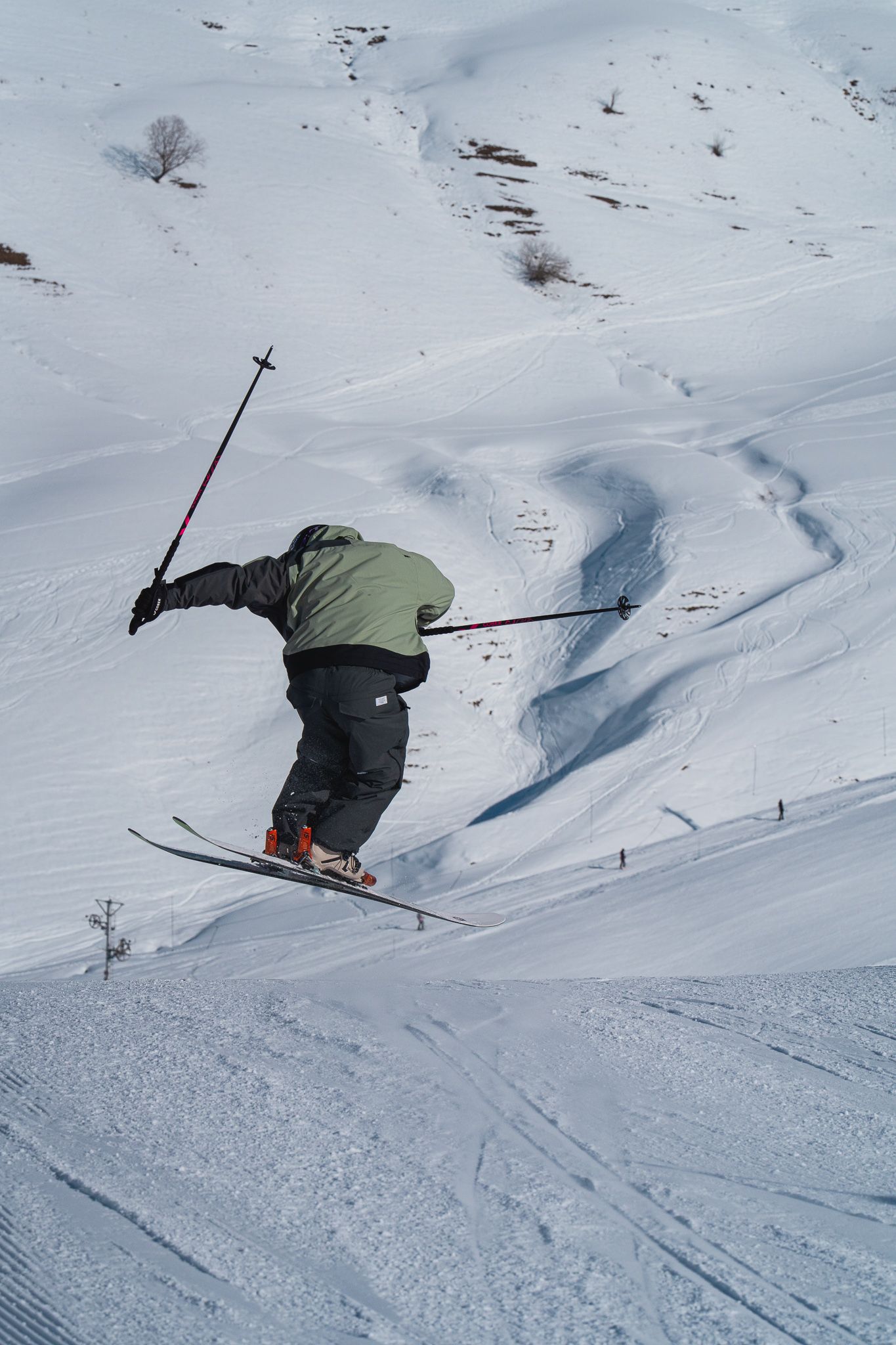 A skier performs a jump on snowy slopes with ski poles extended while carving through fresh powder.