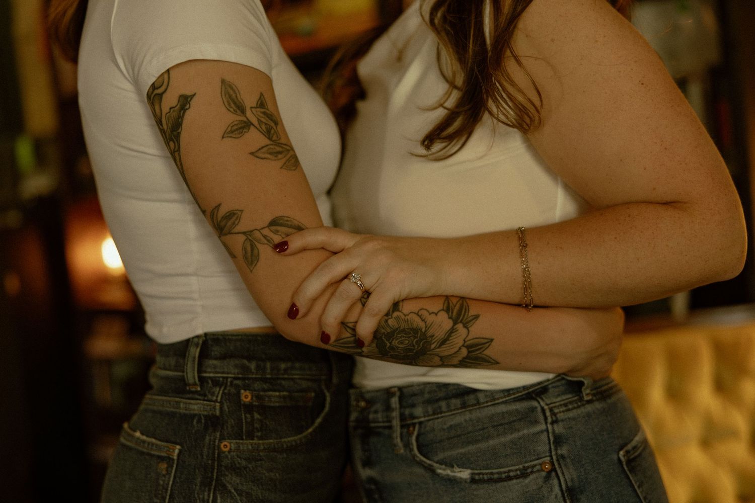 Close-up view of arms with tattoos wearing a white tank top and denim jeans in warm lighting.