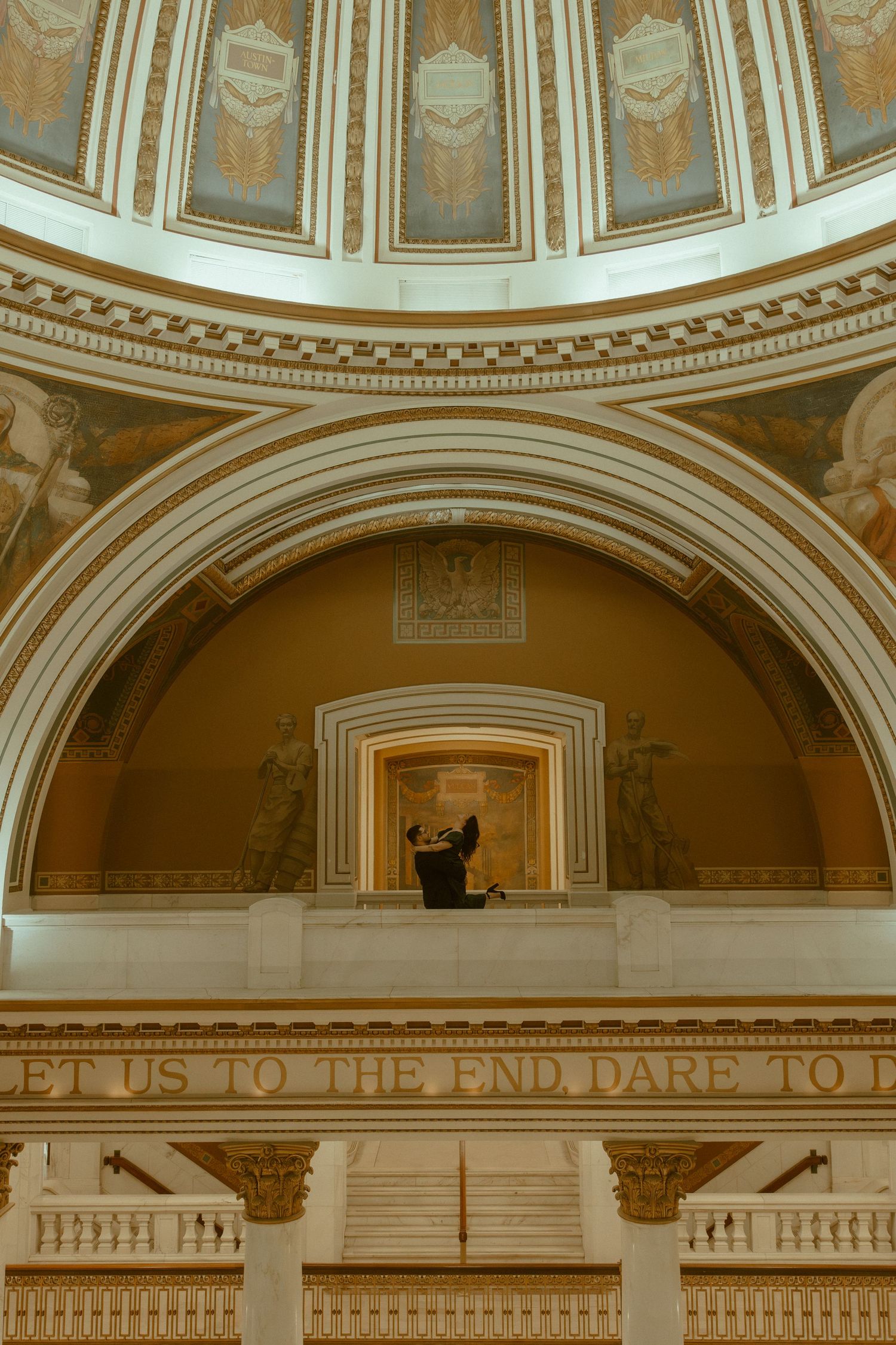 Ornate architectural detail of a classical domed ceiling with decorative moldings and arched columns in warm golden tones.