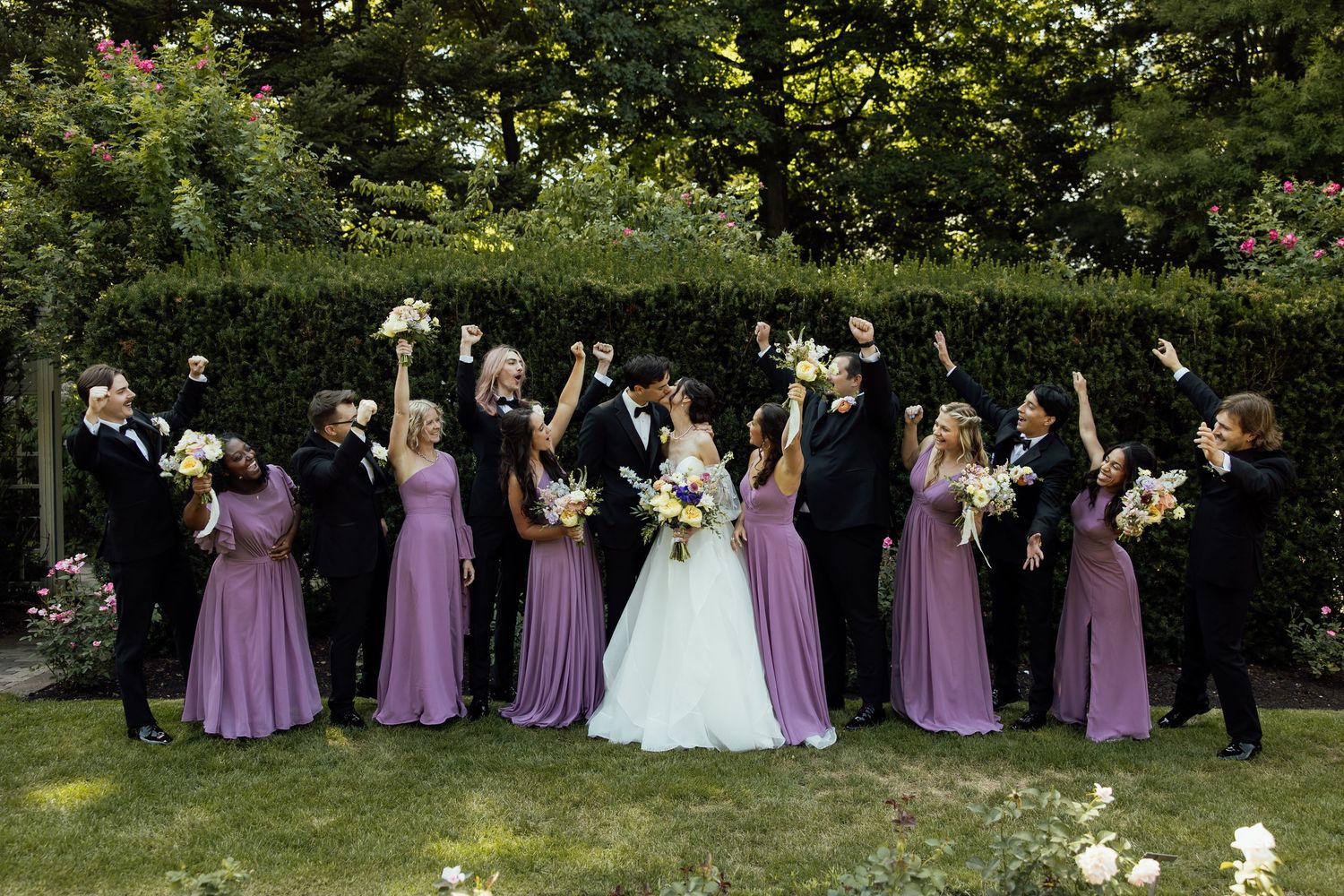 Wedding party in purple bridesmaid dresses and formal attire gathered outdoors for group photos.