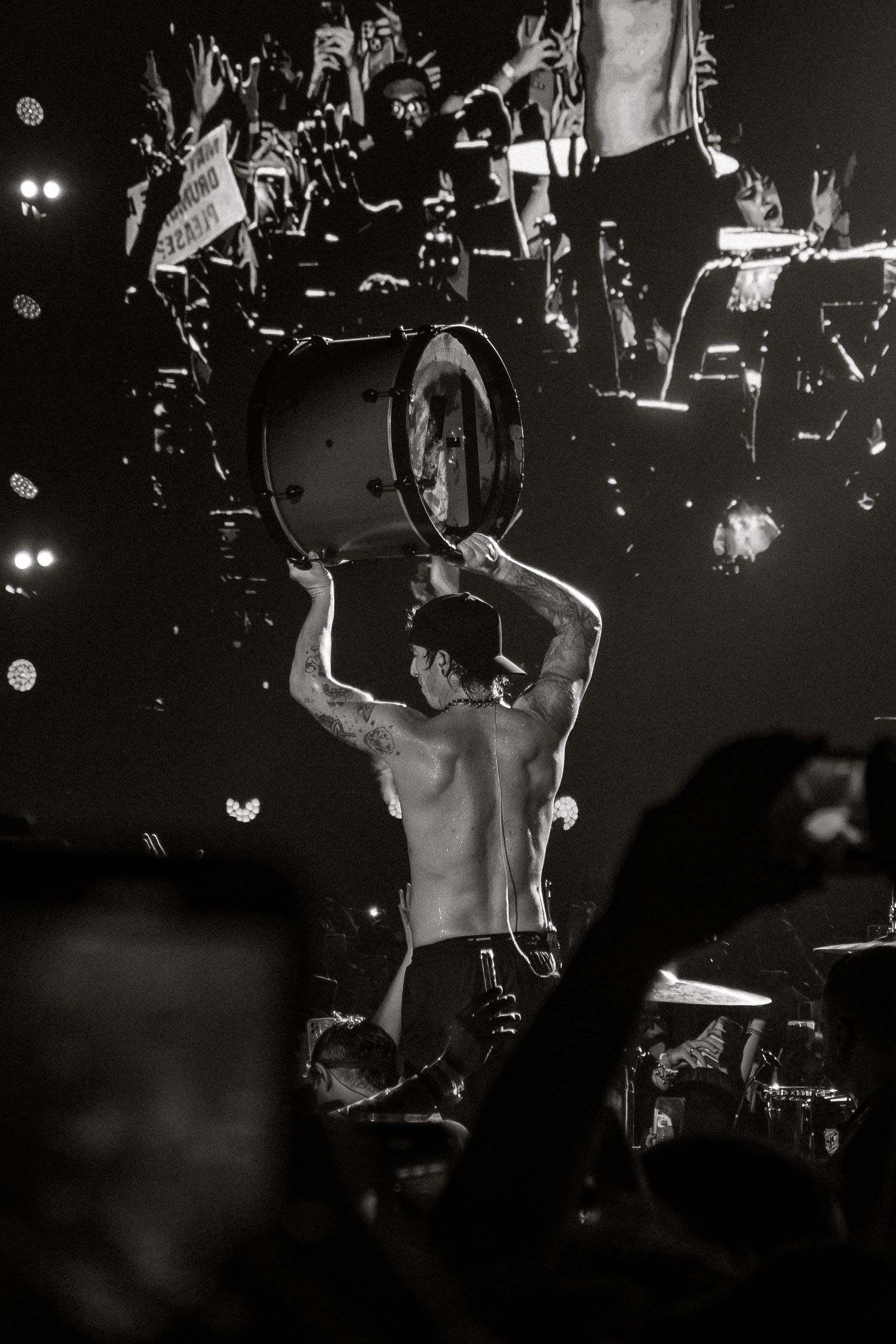 Dramatic black and white concert photo showing silhouetted performer lifting equipment overhead.