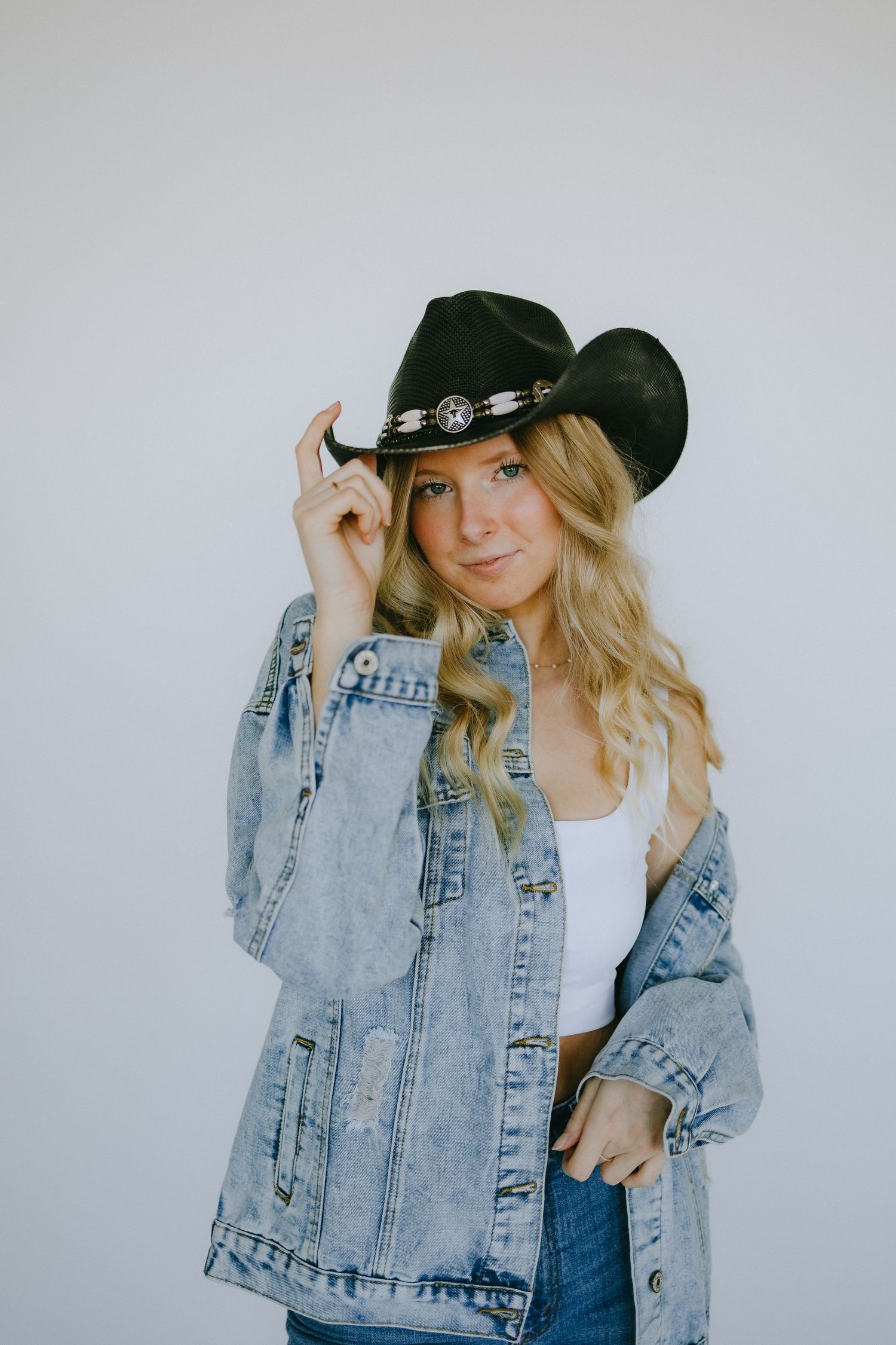 Western-inspired fashion portrait with denim jacket and black cowboy hat.