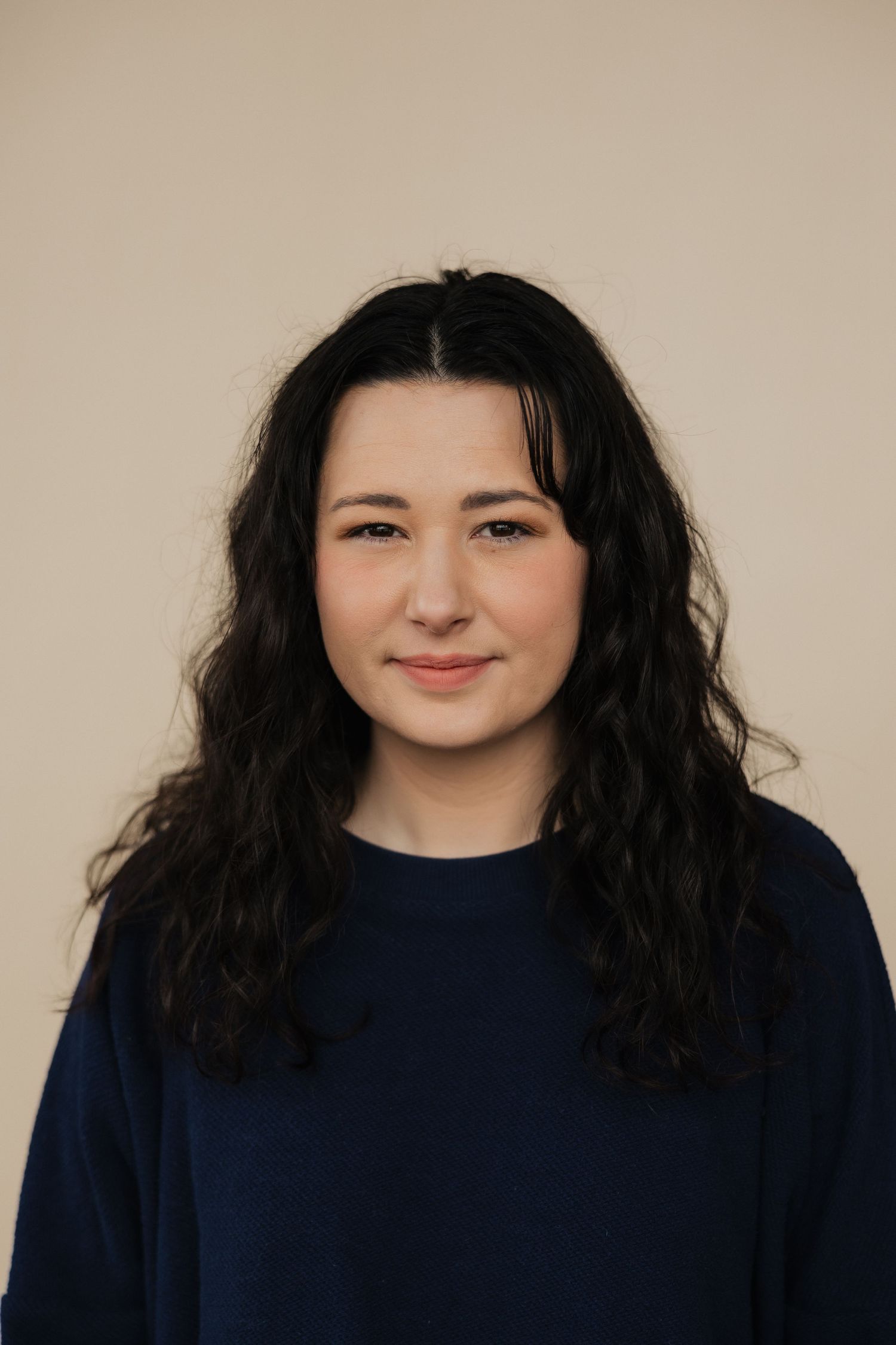 Studio portrait of person in navy sweater against beige background.