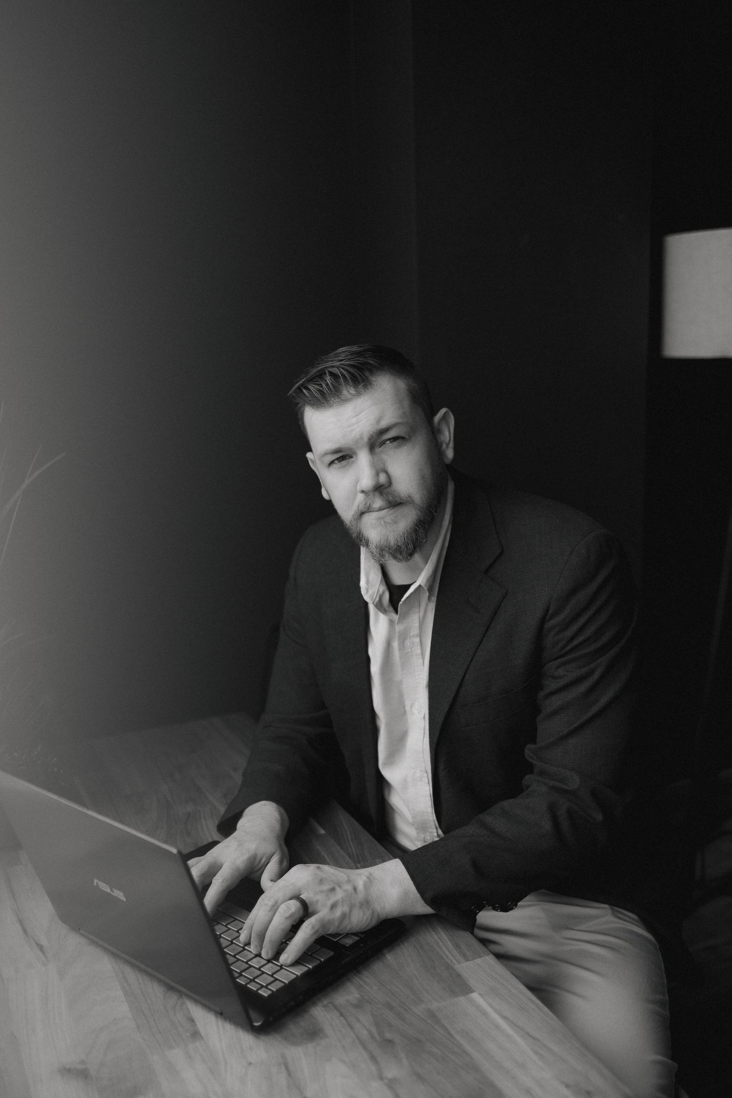 Professional working on laptop in moody lighting against dark background.