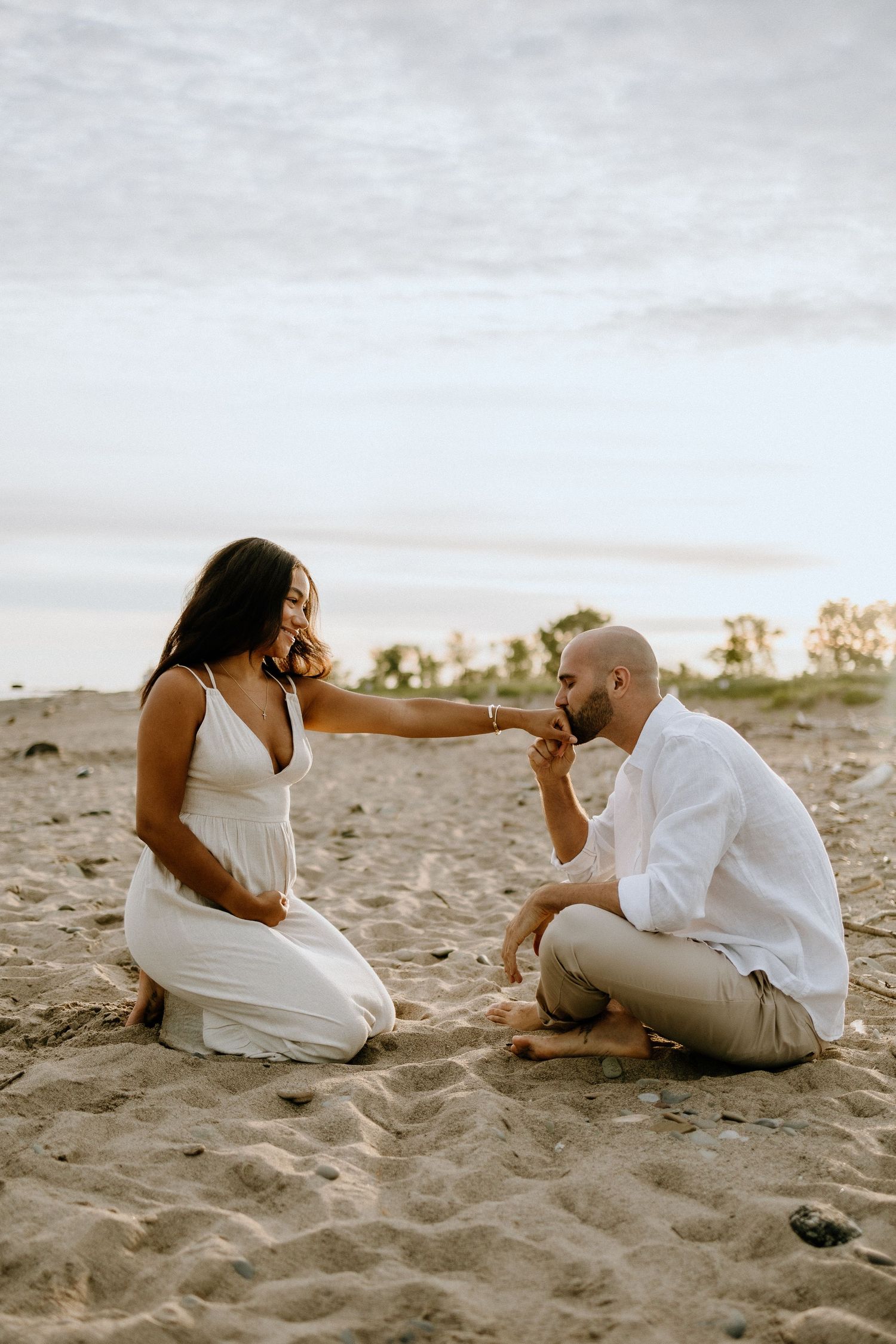 An intimate beach scene showing a romantic moment between a couple in white attire.