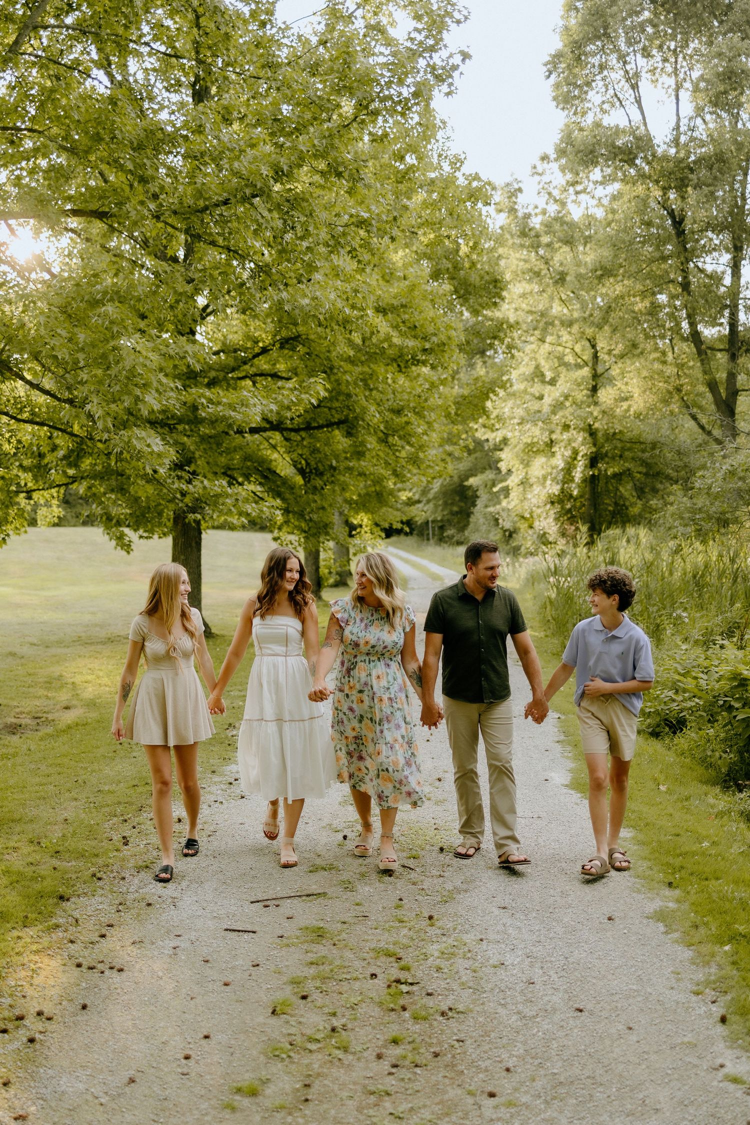 Group walking hand in hand down a tree-lined path on a sunny summer day.