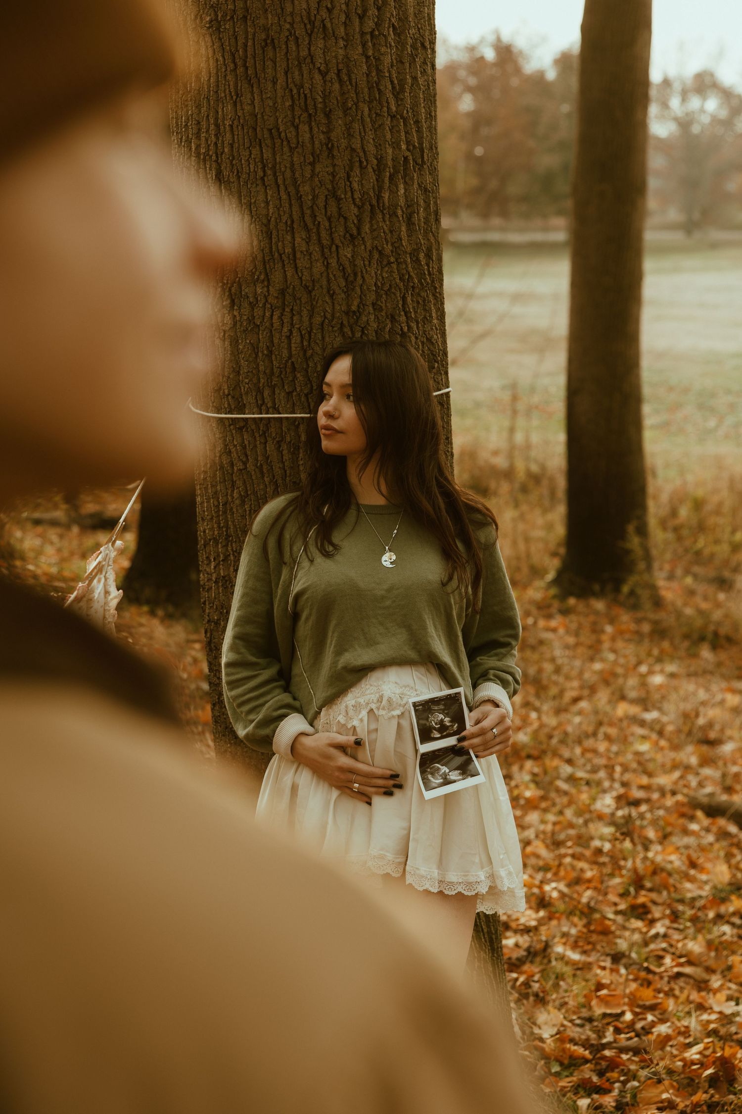 A series of sepia-toned autumn photos showing someone holding ultrasound images among fallen leaves and trees.