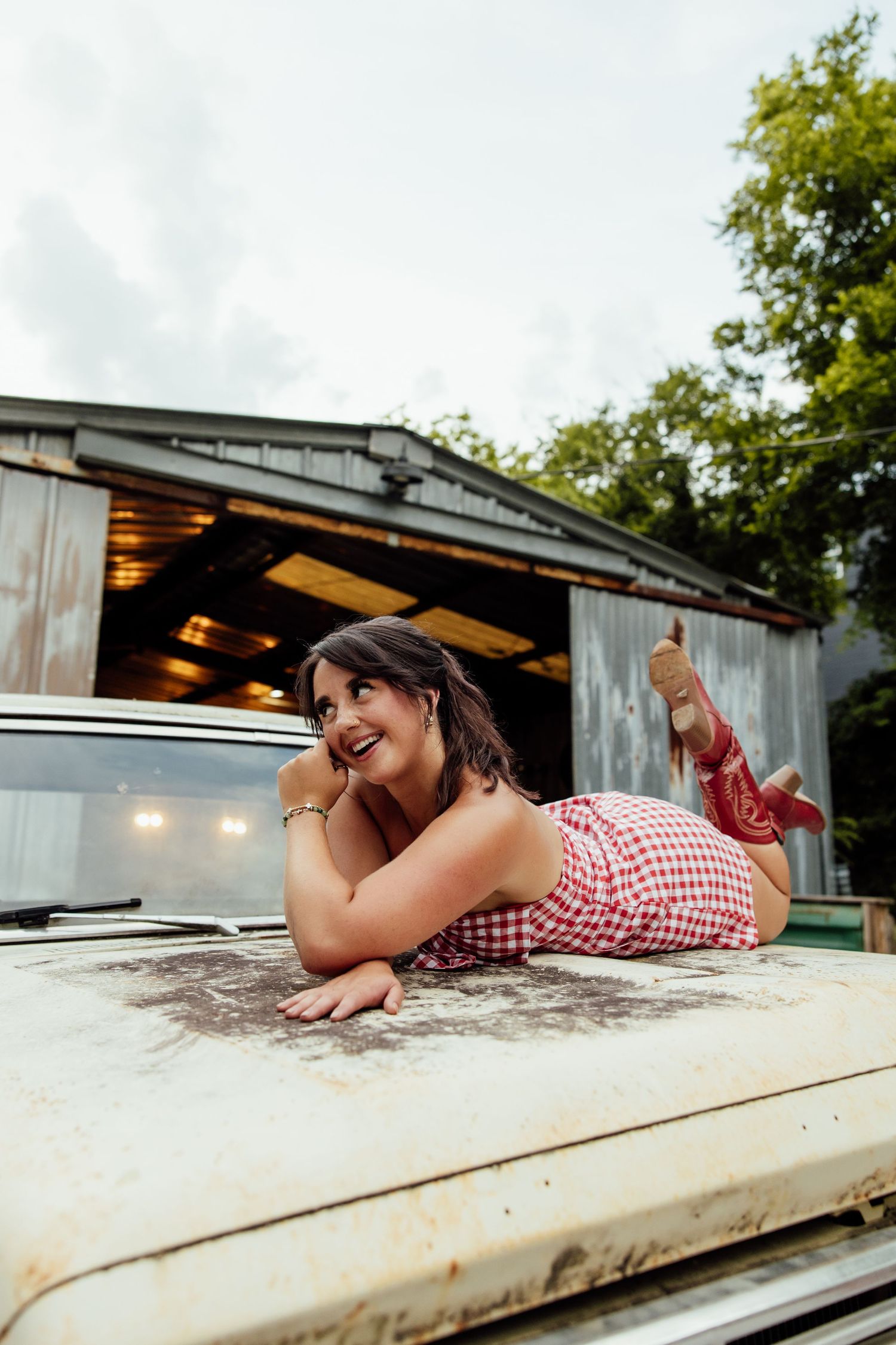 A person in a red and white gingham dress lies playfully on a wooden deck during a sunny summer day.