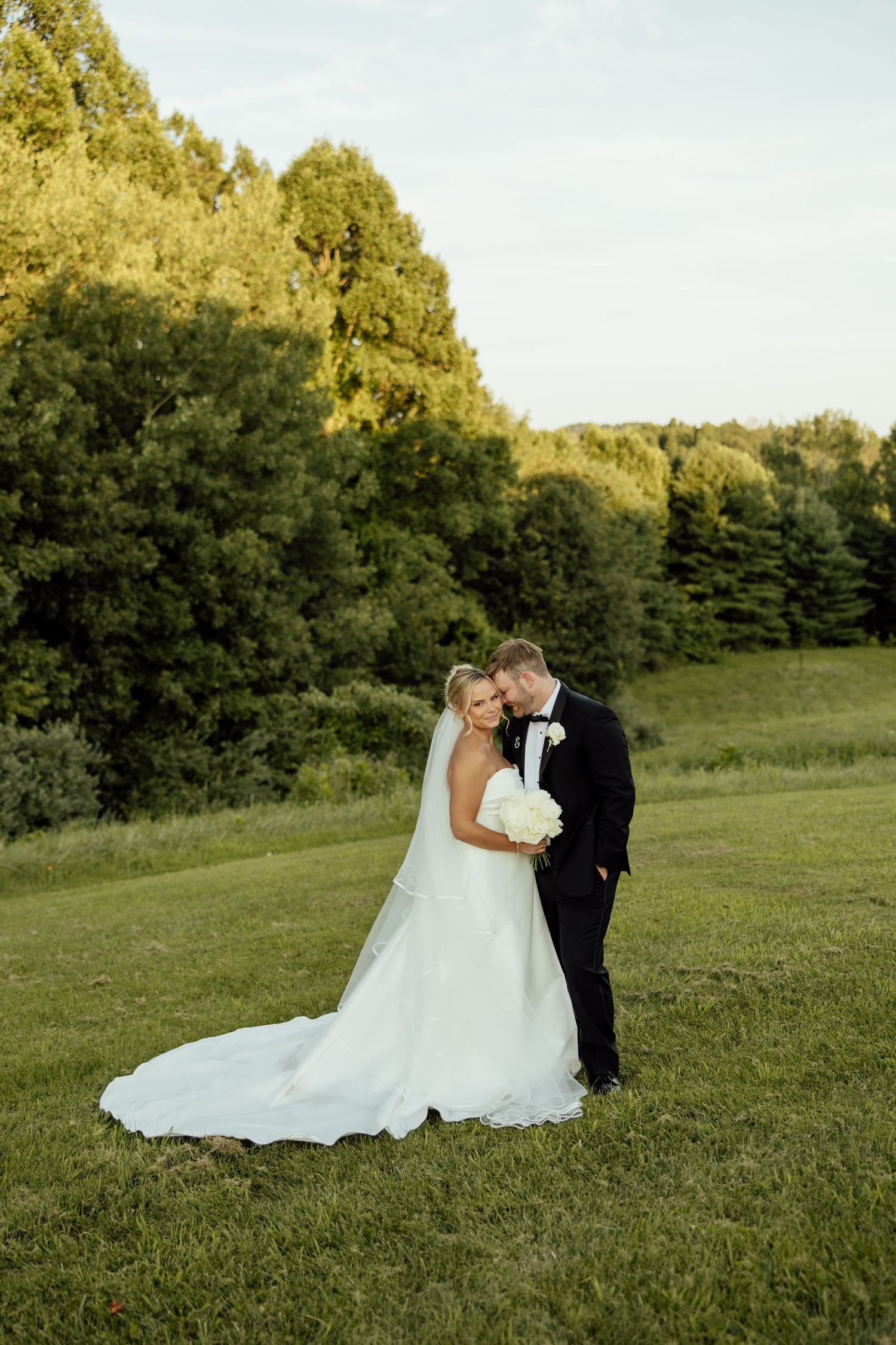 A romantic wedding couple shares an intimate moment together on a grassy hillside at golden hour.